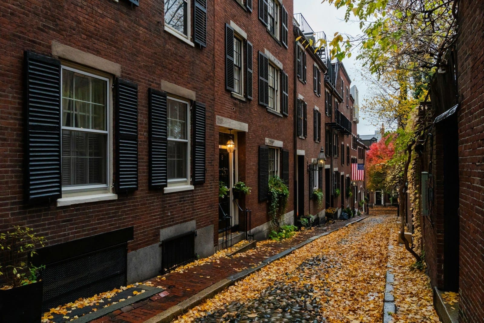 La pittoresque Acorn Street dans le quartier Beacon Hill de Boston, avec ses maisons en rangée en brique, ses volets noirs, ses pavés en pierre et ses feuilles d'automne dispersées sur le trottoir.