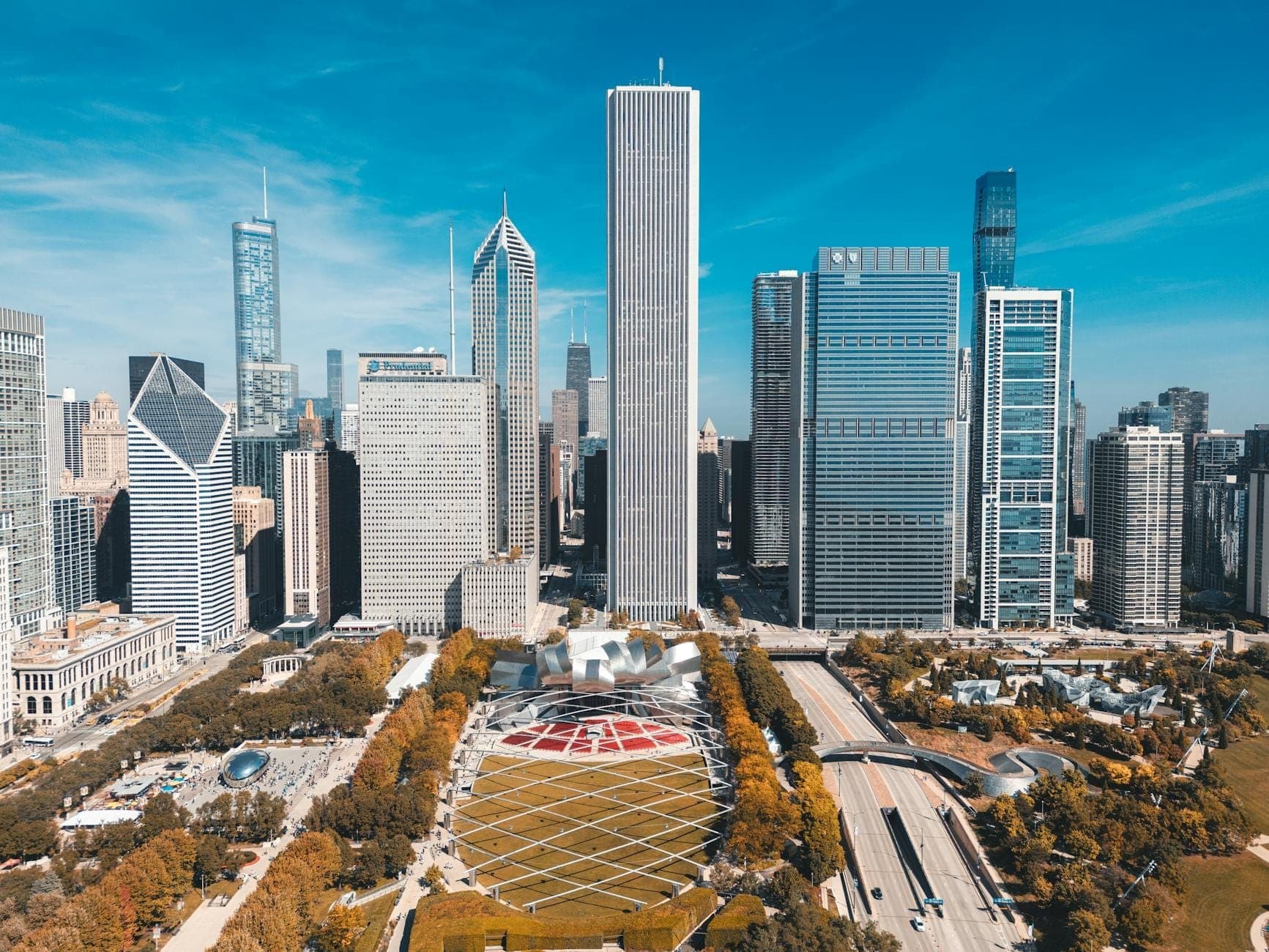 Aerial view of Chicago's Loop skyline with skyscrapers, Millennium Park, and Grant Park visible under a clear blue sky.
