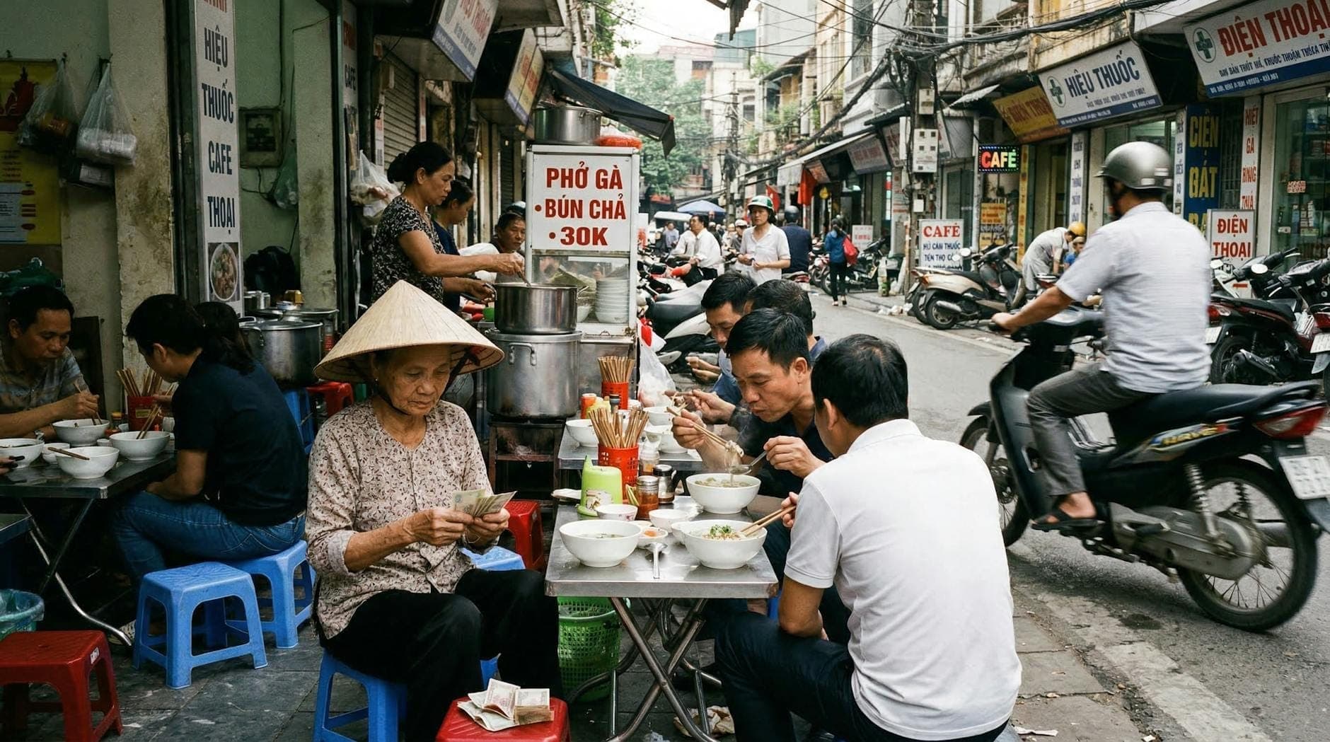 Concurrida calle del Casco Antiguo de Hanoi con lugareños comiendo en puestos de comida en la acera, scooters pasando y tiendas a lo largo de estrechas y animadas calles