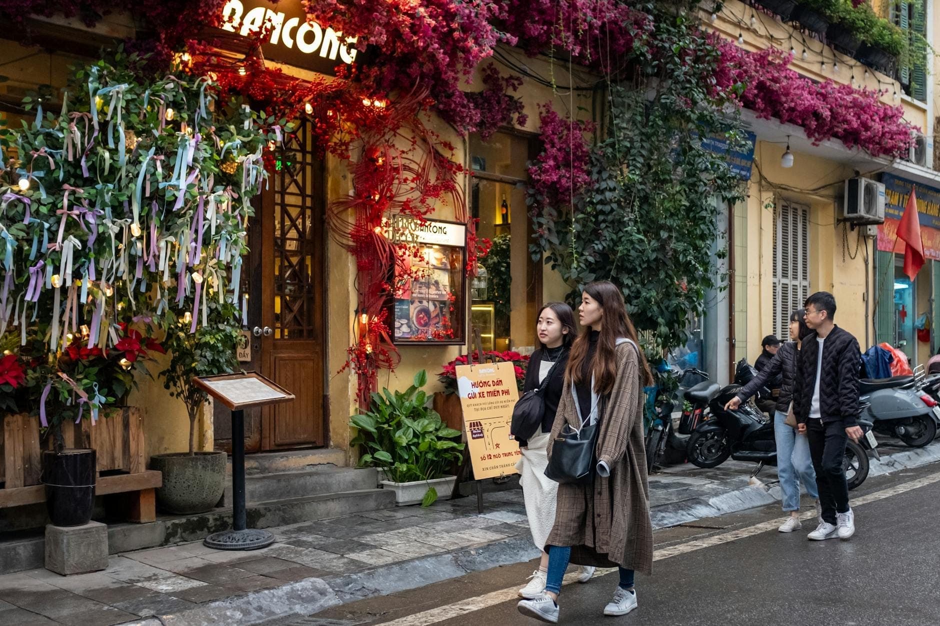 Ludzie spacerujący ruchliwą ulicą Hanoi przyozdobioną kolorowymi kwiatami i tętniącymi życiem lokalnym sklepami – klimat i urok dzielnic wietnamskiej stolicy.