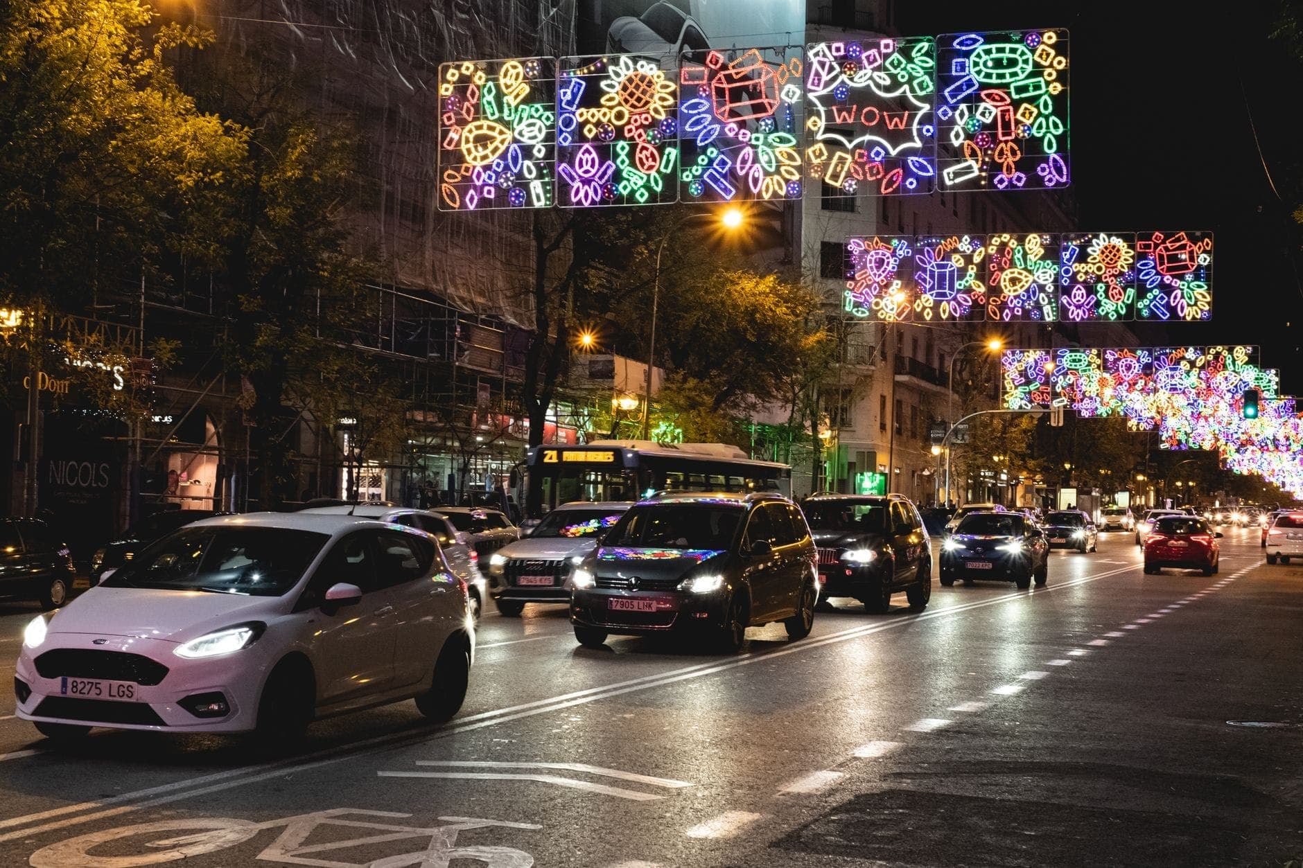 Trafficata strada di Madrid di notte con luci al neon colorate, auto di passaggio e vivace energia cittadina.