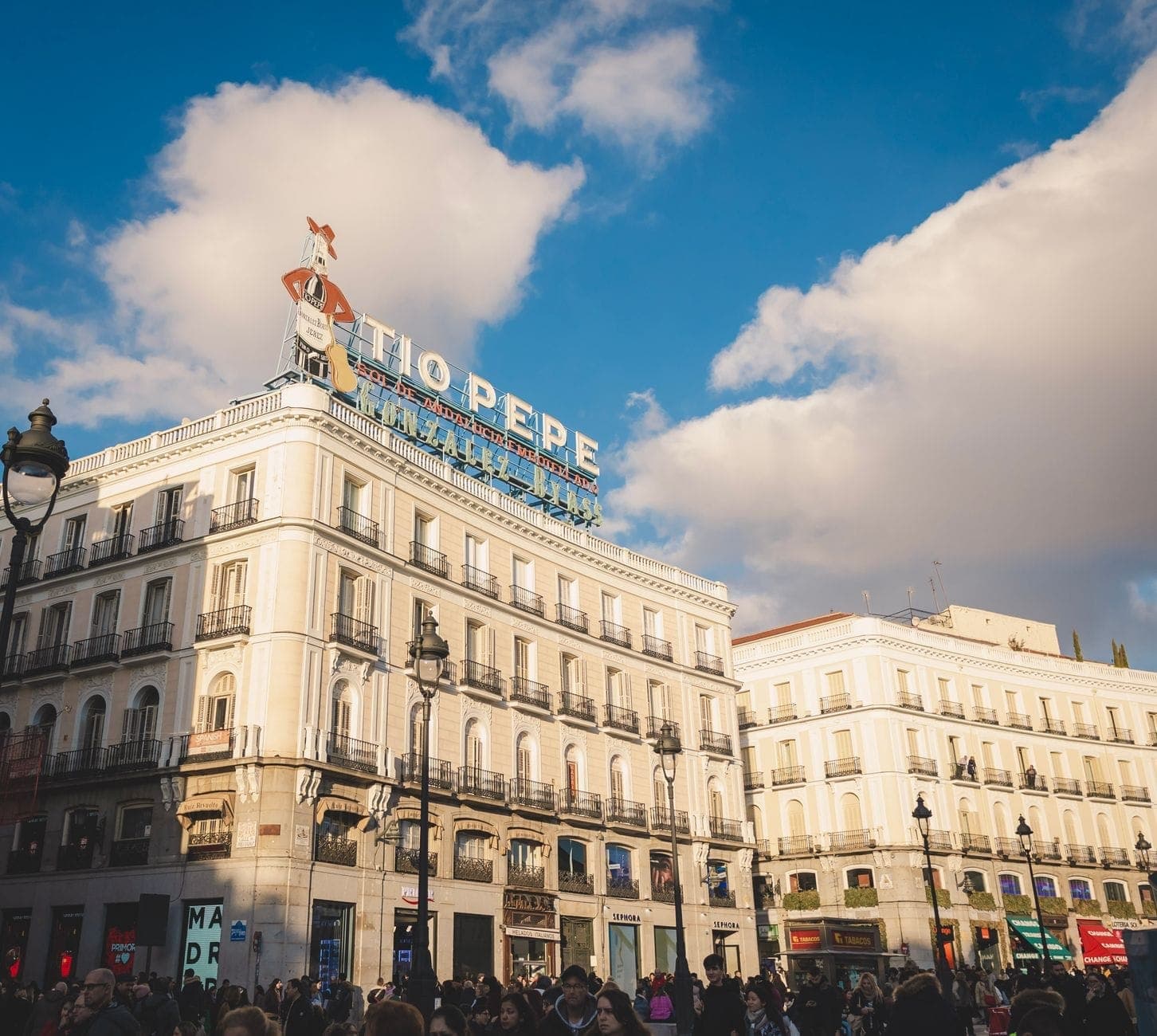 Piazza affollata a Madrid con l'iconico cartello Tio Pepe su un edificio storico sotto un cielo azzurro