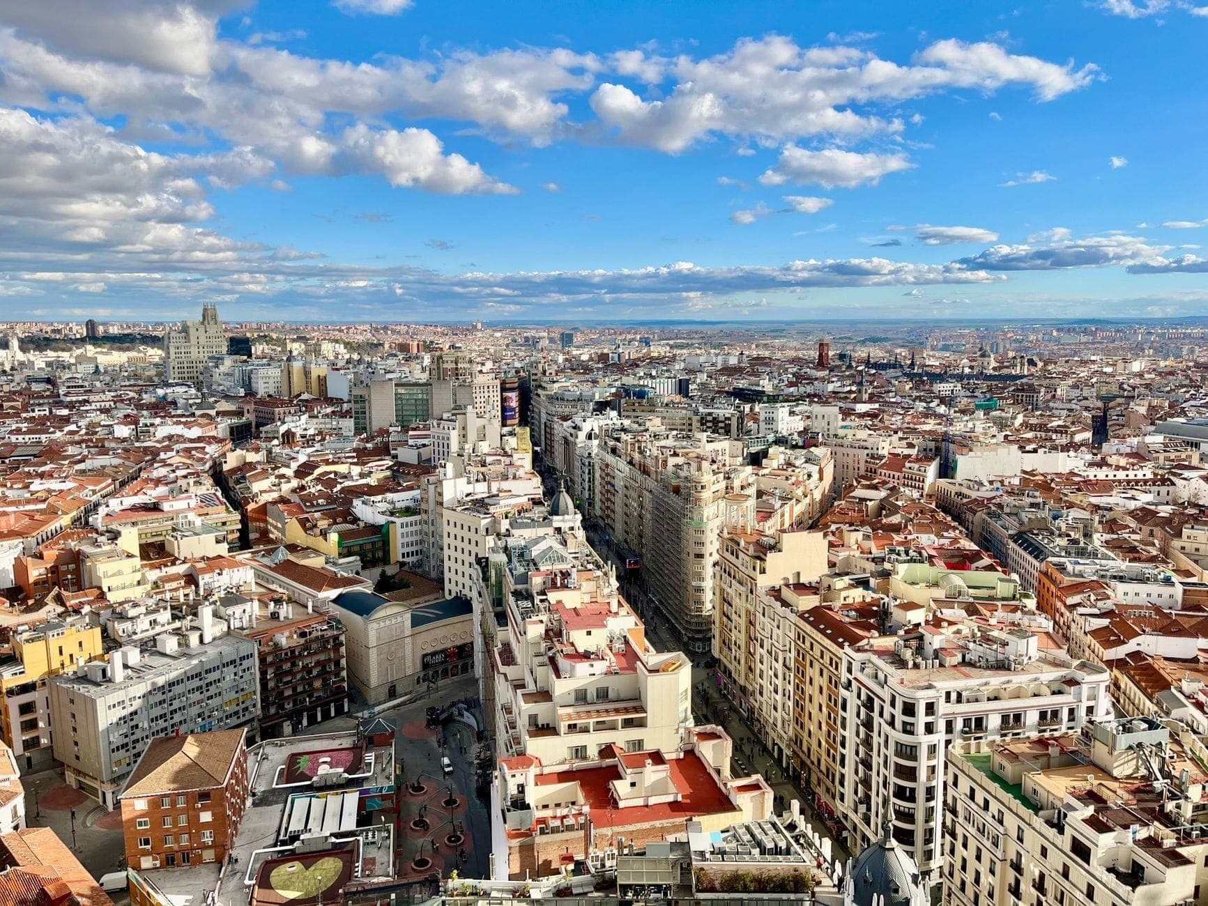 Vista panoramica sul centro di Madrid con quartieri variegati, edifici e la vivace Gran Vía sotto un cielo azzurro.