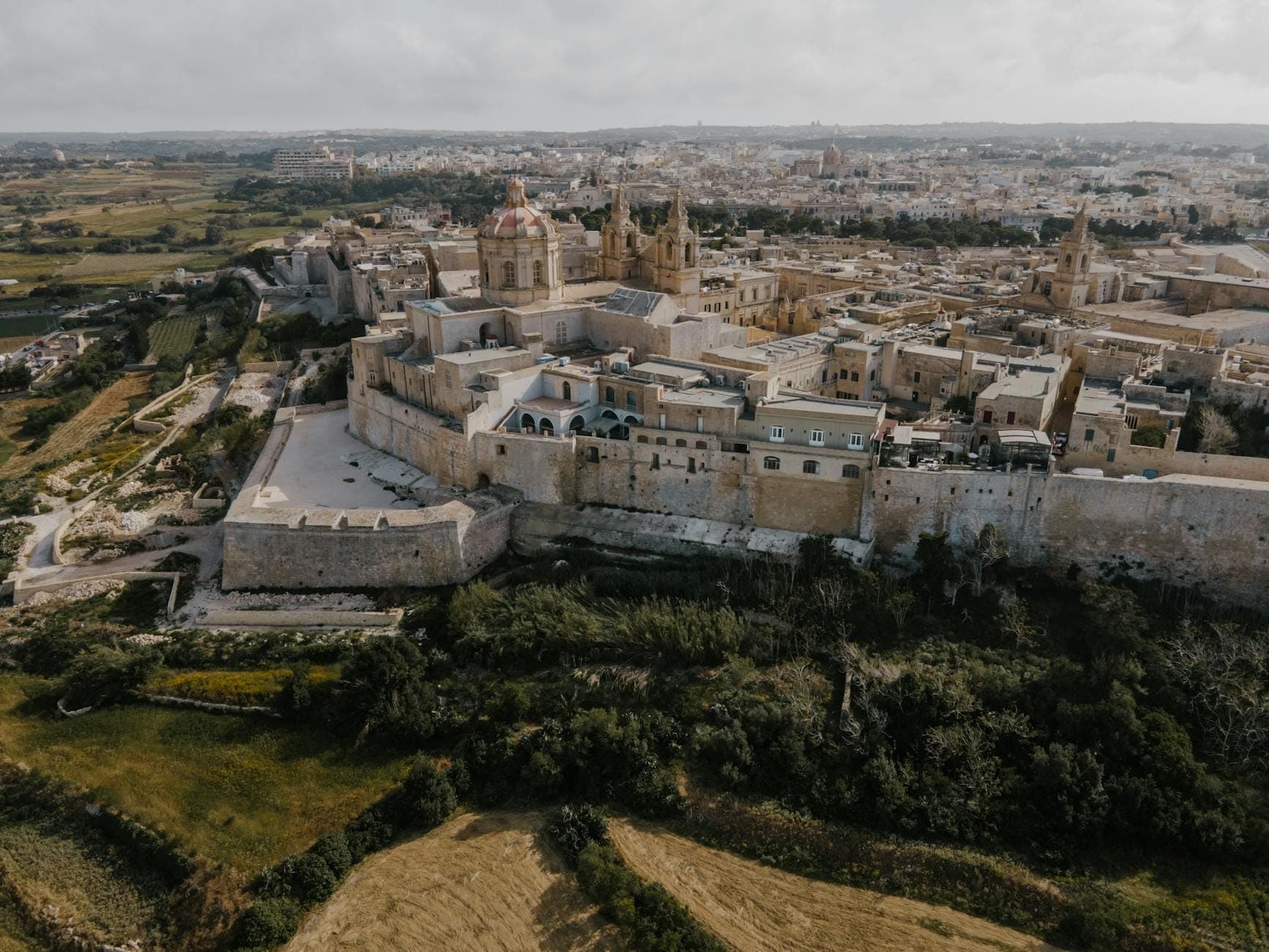 Luftaufnahme von Mdina, Maltas ummauerte mittelalterliche Stadt, mit alten Steinmauern, Kathedralen und historischen Gebäuden inmitten der Landschaft.