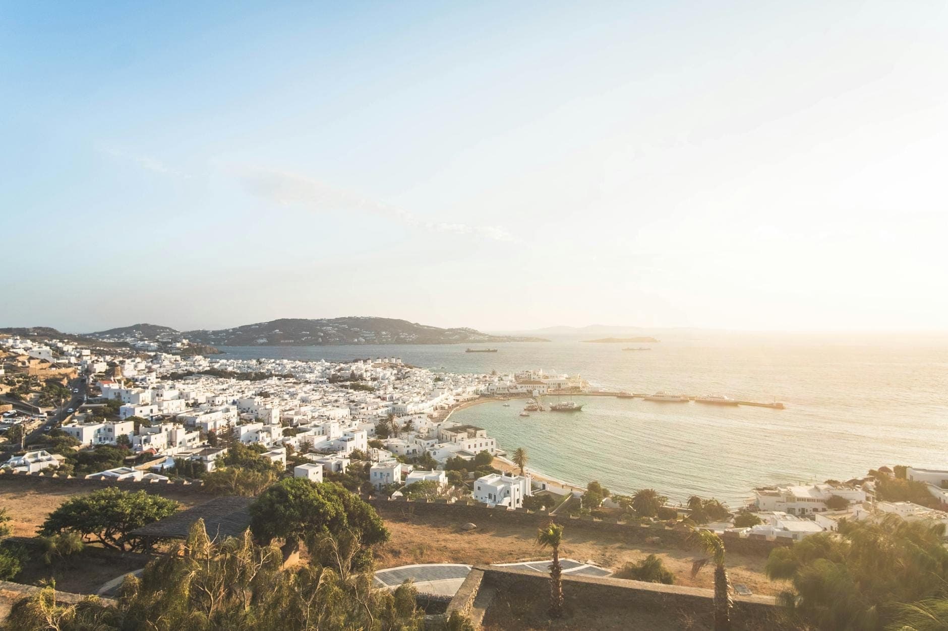 Weitläufige erhöhte Ansicht von Mykonos-Stadt, Küstenlinie und Hafen mit weißen Gebäuden und Hügeln, ideal um die Anordnung der Insel zu verstehen