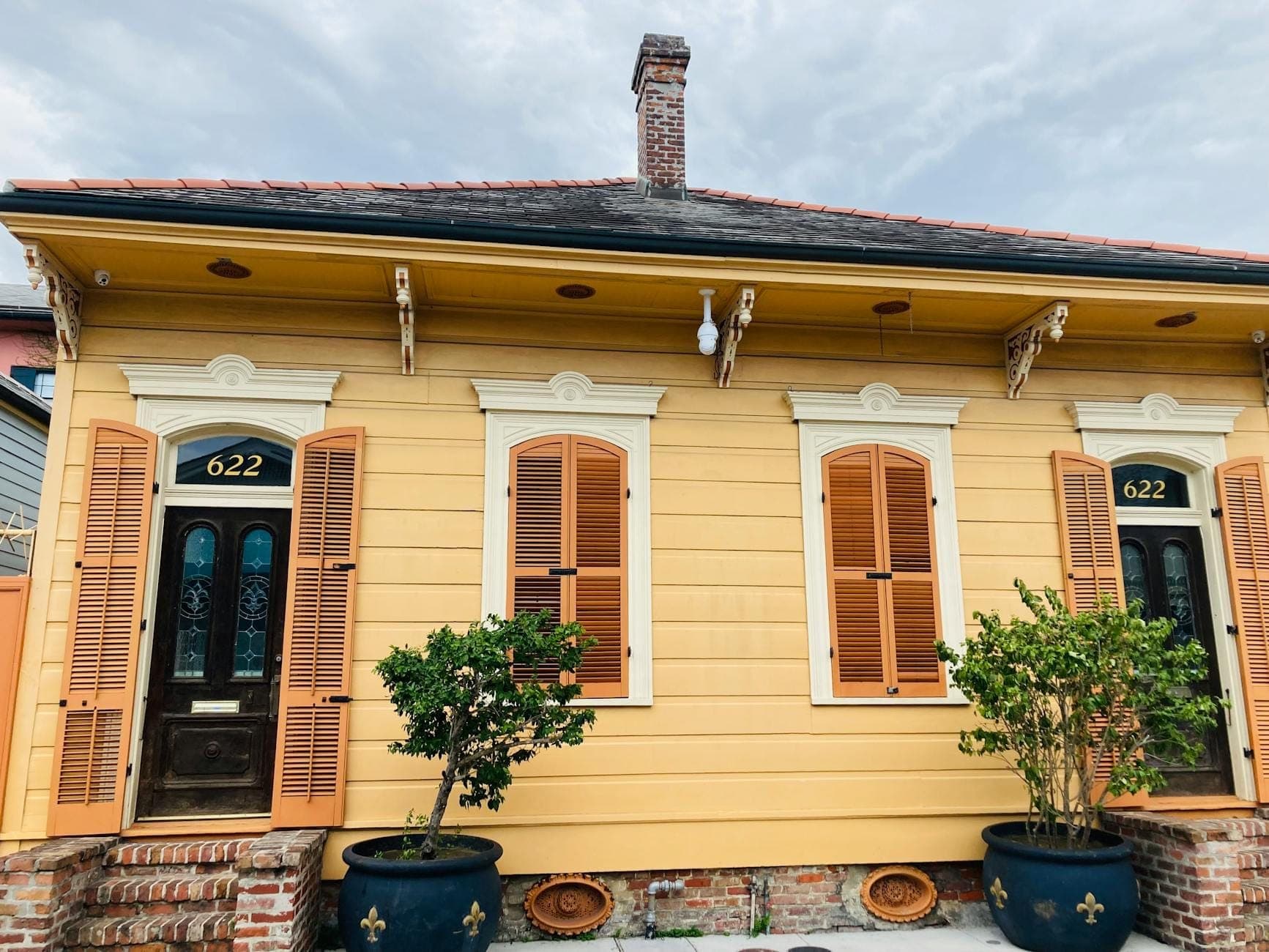 Maison shotgun historique de la Nouvelle-Orléans avec façade jaune vif, volets classiques et portes jumelles, dégageant le charme unique d'un quartier local.