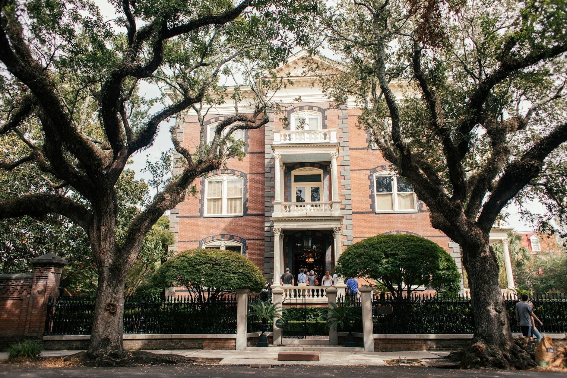 Grande demeure antebellum dans le Garden District de La Nouvelle-Orléans avec une façade en brique, un porche avant, une clôture en fer forgé et des chênes vivants encadrant l'entrée.