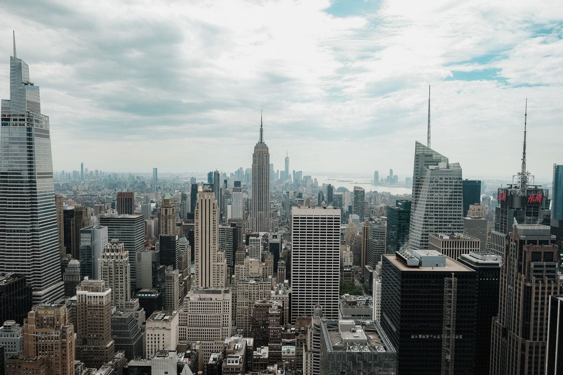 วิวกว้างของเส้นขอบฟ้า Midtown Manhattan พร้อม Empire State Building และตึกระฟ้าใต้ท้องฟ้ามีเมฆบางส่วน