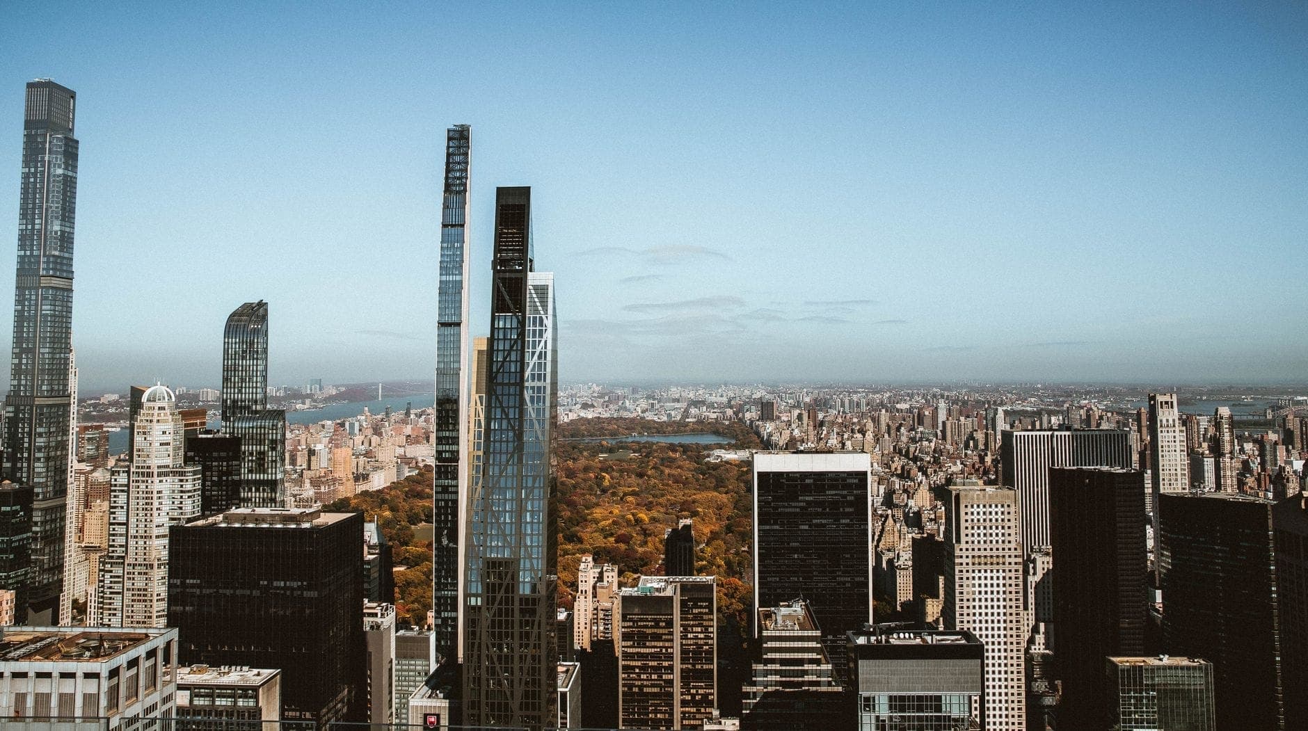 วิวกว้างของกลุ่มตึกสูง Midtown Manhattan มองเห็น Central Park อยู่ไกลๆ ใต้ท้องฟ้าสีฟ้าใส ครอบคลุมบรรยากาศโยงหลายย่านในนิวยอร์กซิตี้