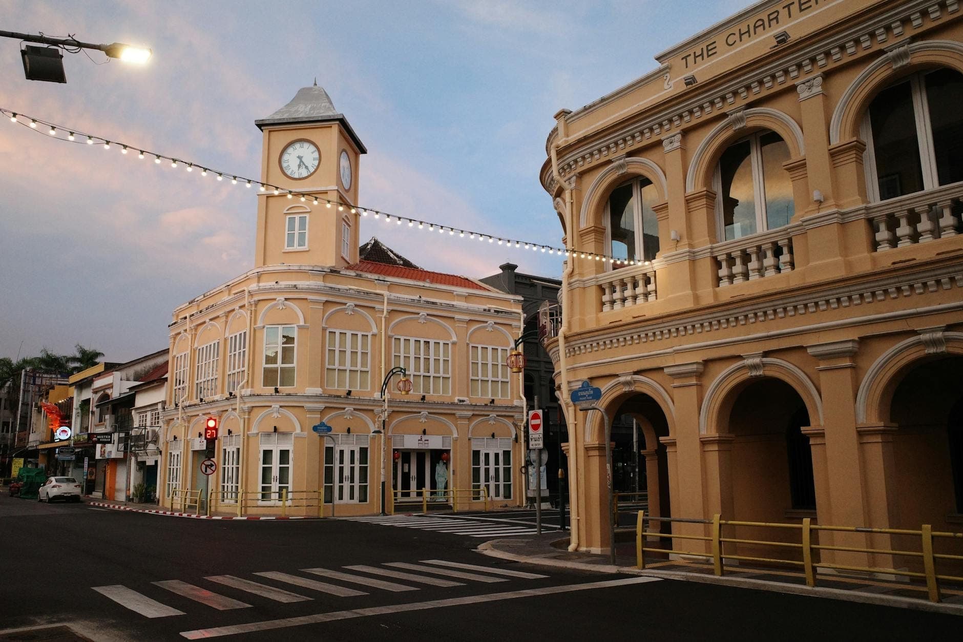 Tahimik na sulok ng kalye sa Phuket Old Town sa takipsilim, na may kolonyal na arkitektura, dilaw na gusaling may torre ng orasan, at mga arched na balkonahe.