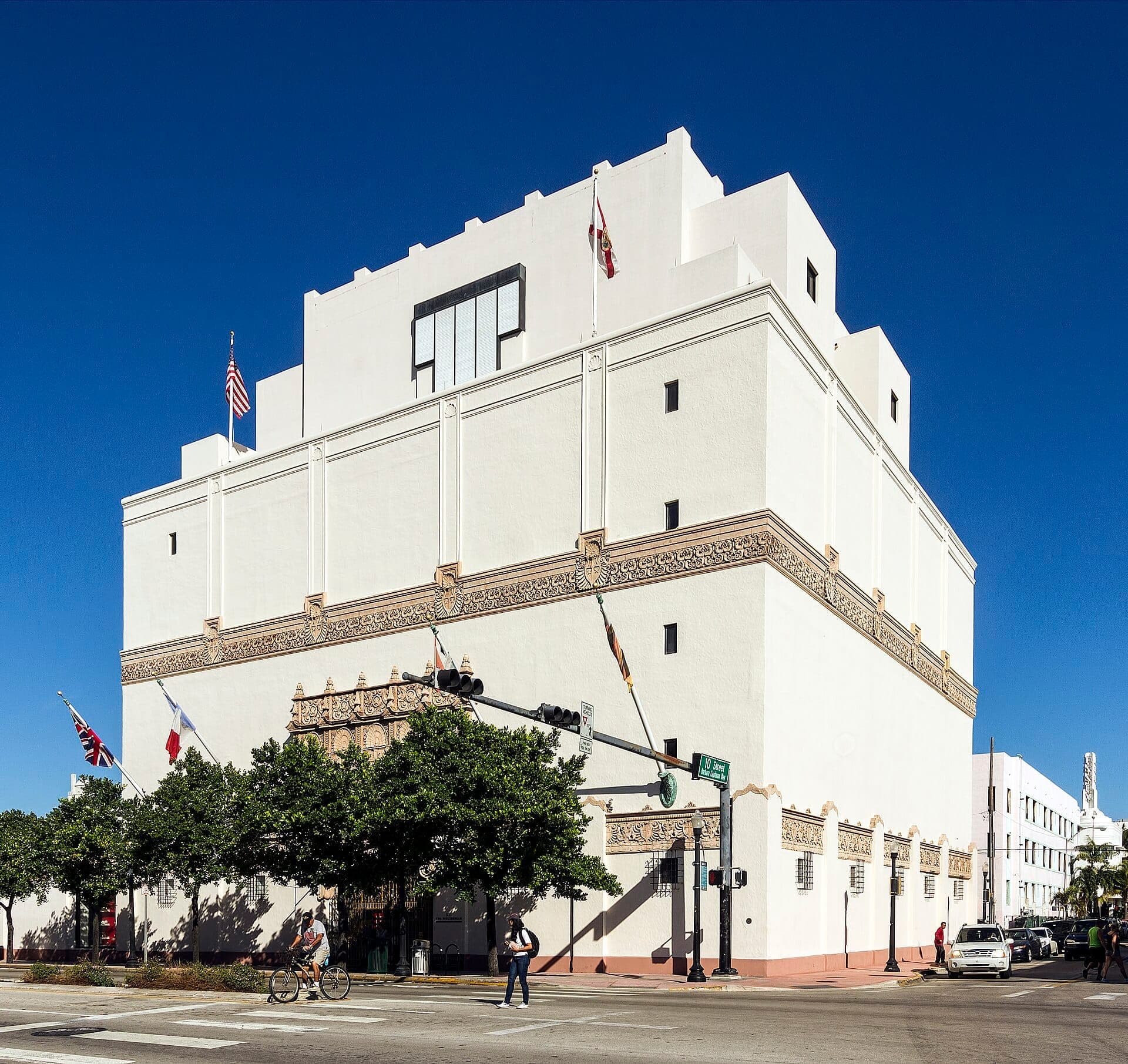 Extérieur du musée Wolfsonian–FIU à Miami Beach, montrant son architecture blanche de style Renaissance méditerranéenne, des drapeaux et un ciel bleu ensoleillé.