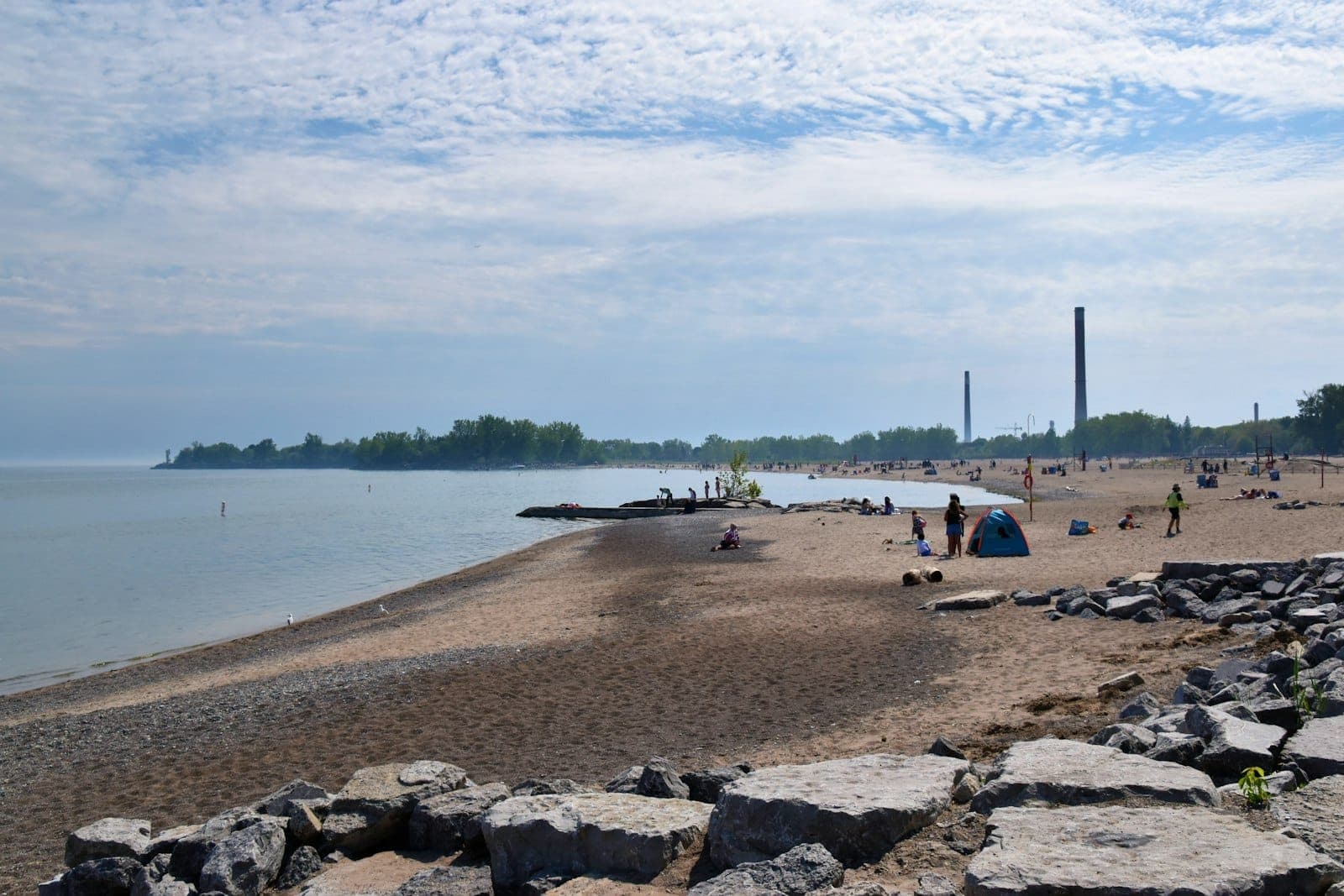 Vista ampia di Woodbine Beach con la riva sabbiosa, le acque calme del lago, gente che si rilassa e un cielo parzialmente nuvoloso: la fuga urbana sul lago di Toronto.