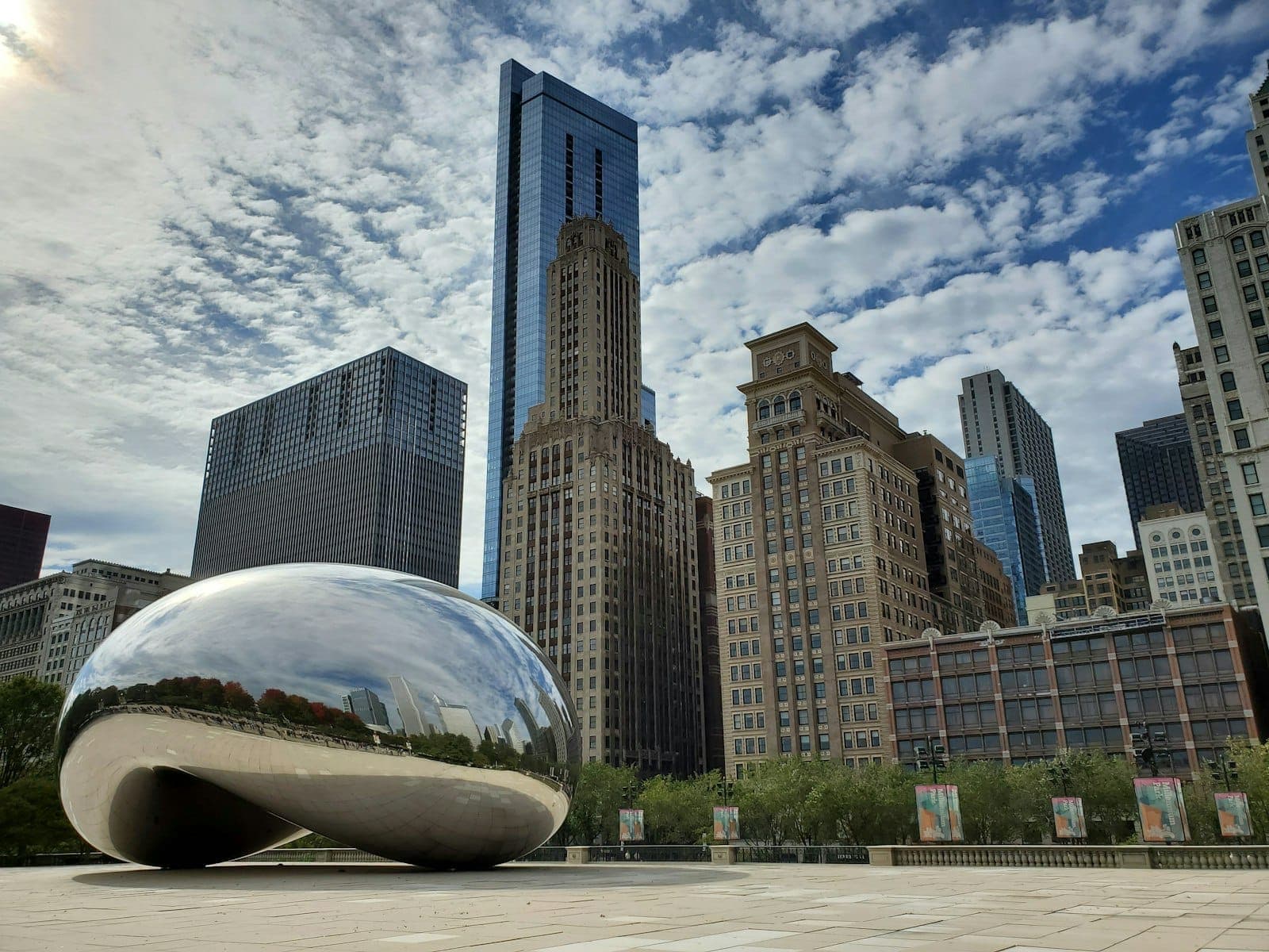 Una vista clara de Cloud Gate (el Frijol) en Millennium Park Chicago, con rascacielos de la ciudad al fondo bajo un cielo azul con nubes dispersas.
