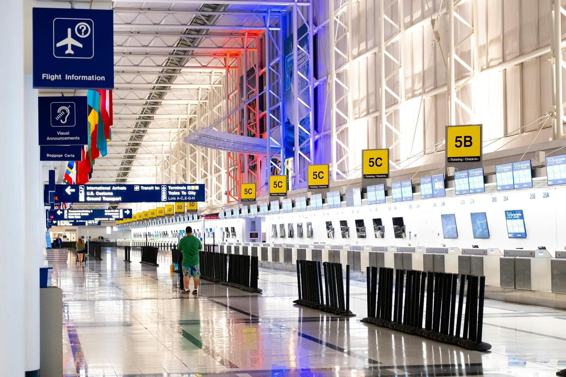 Vista amplia de los mostradores de facturación del aeropuerto O'Hare con señales de vuelo, iluminación colorida y banderas internacionales en lo alto.