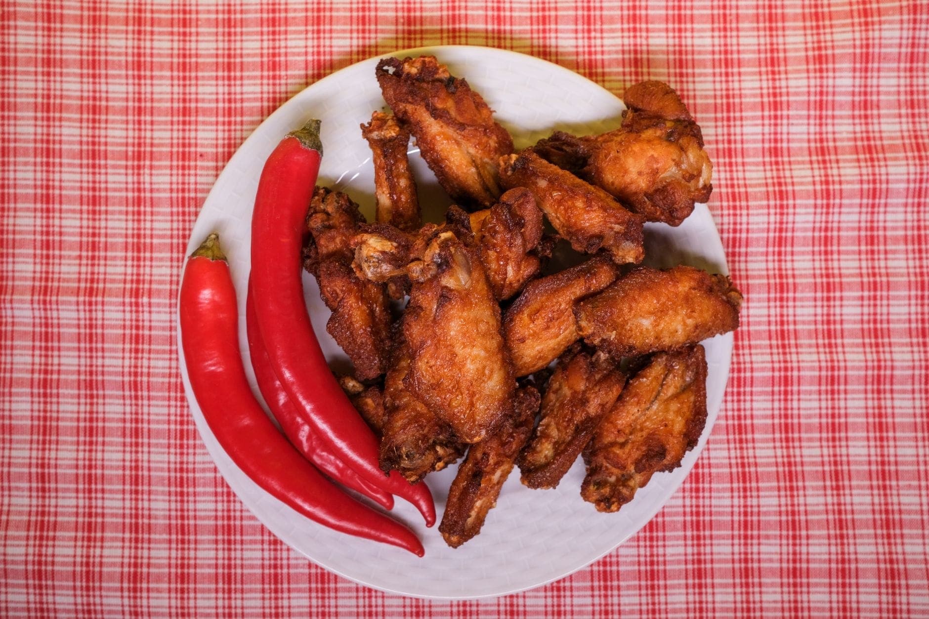 Talerz chrupiących smażonych skrzydełek z kurczaka i czerwonych papryczek chili na kratowanym obrusie, przywołujący klasyczny Nashville hot chicken.