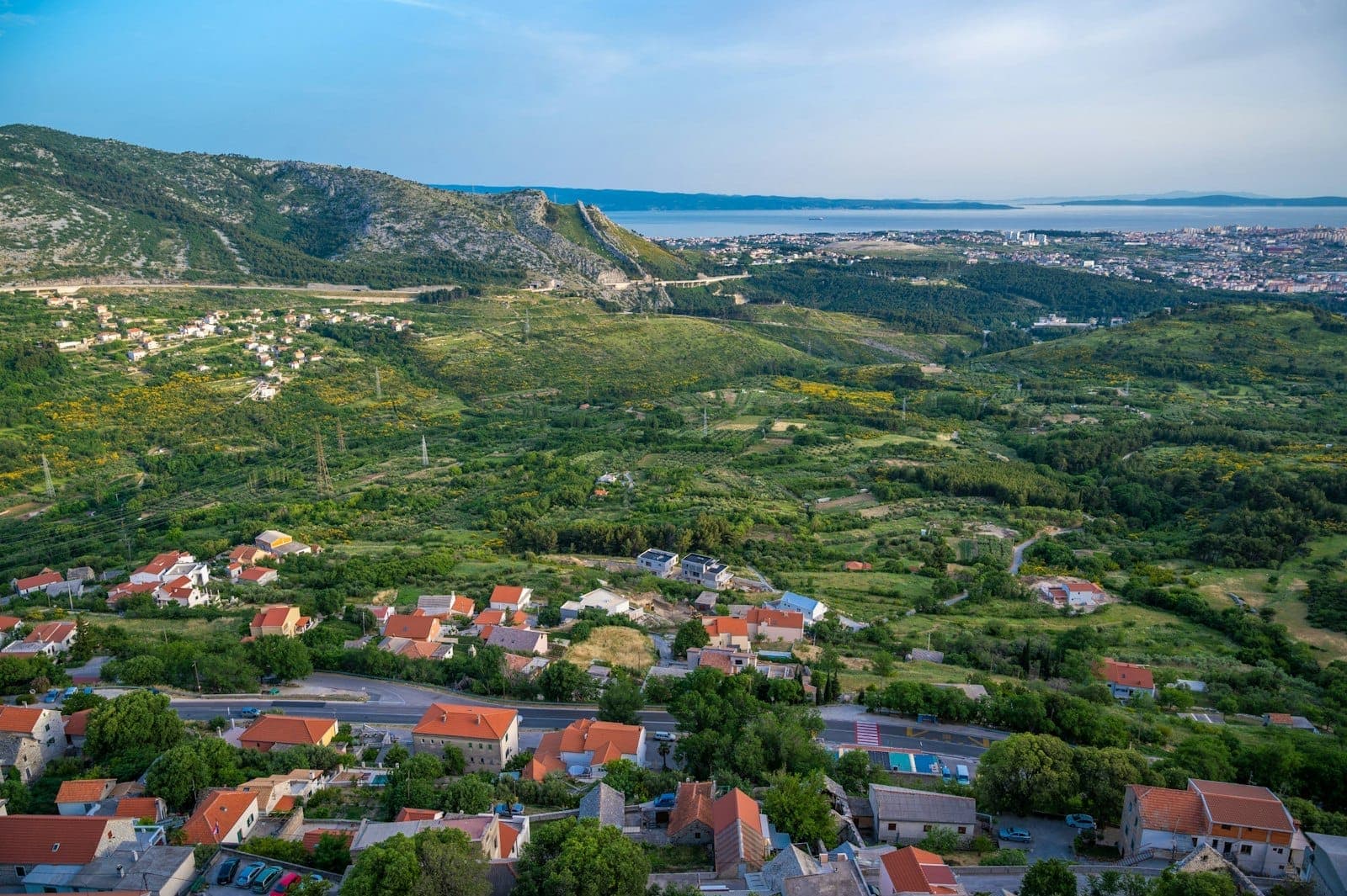 Vista panoramica di una valle verde con case sparse e montagne, che mostra probabilmente l'area intorno a Spalato e possibili destinazioni per gite di un giorno.