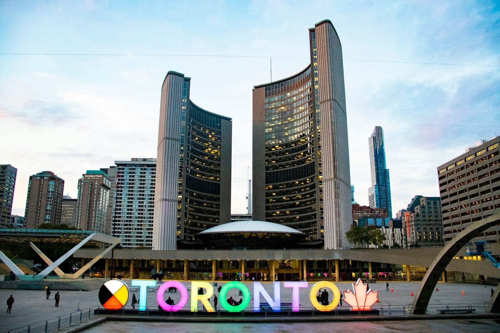 Il Toronto City Hall e il colorato cartello illuminato di Toronto a Nathan Phillips Square, con gli edifici della città sullo sfondo al crepuscolo.