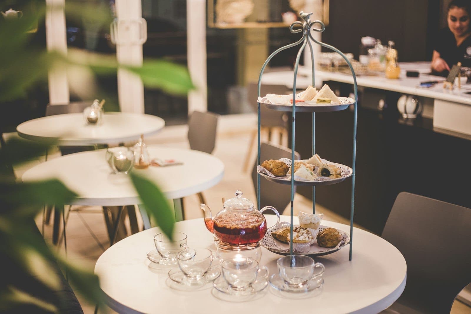 Tavolo di un moderno caffè a Londra apparecchiato con alzatina per afternoon tea, teiera e tazze da tè, in un ambiente rilassato e ben illuminato.