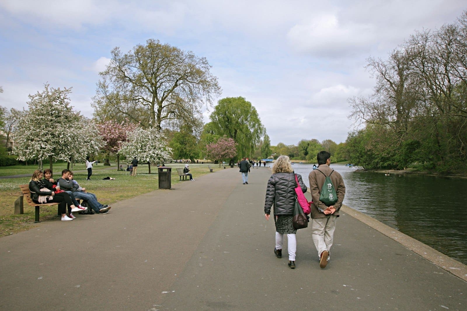 Persone che passeggiano e si rilassano accanto al lago in un grande parco di Londra con fiori primaverili e vialetti aperti.