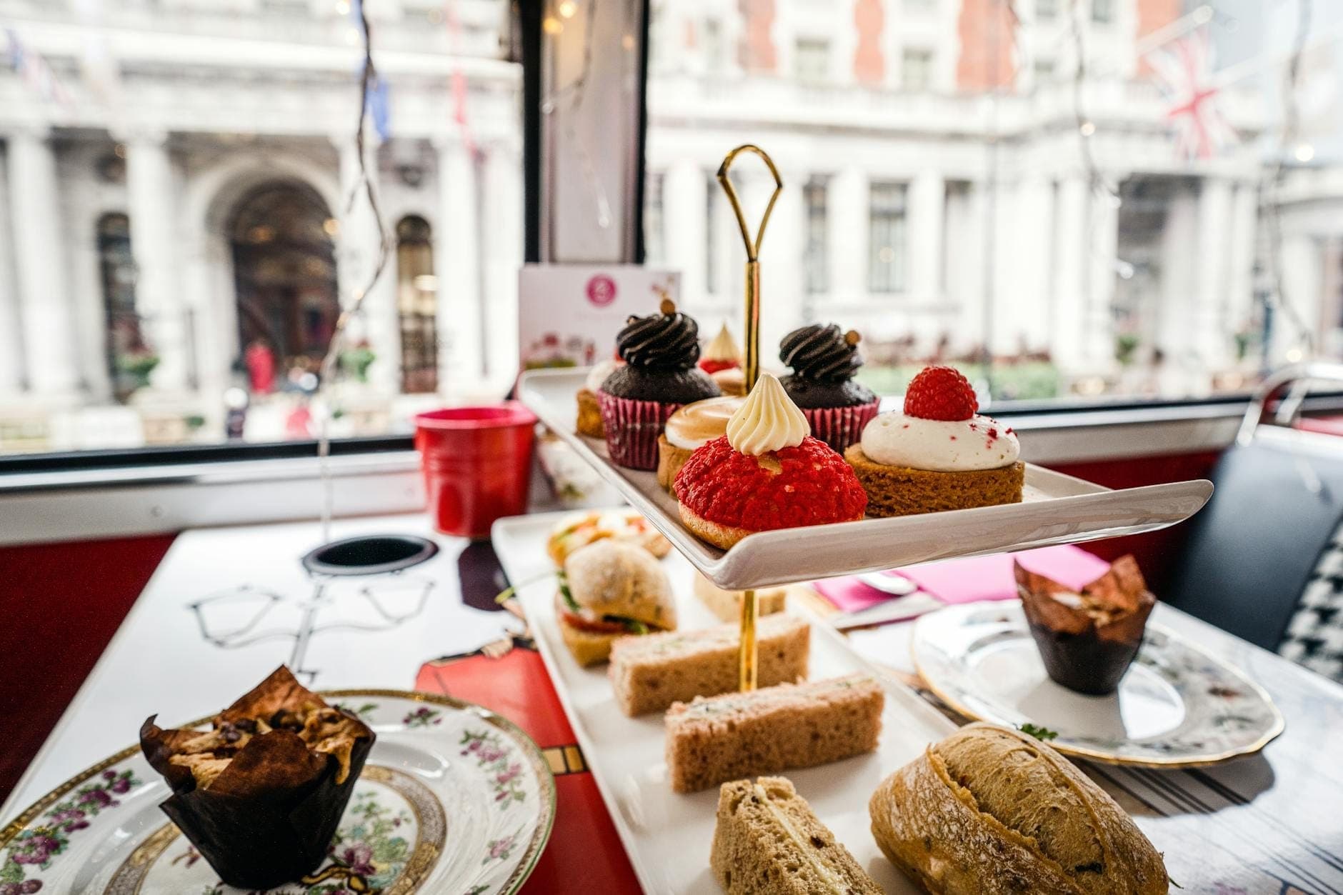 Alzata a tre piani con scones, finger sandwich e pasticcini su un tavolo vicino a una finestra con vista sull'architettura classica di Londra.