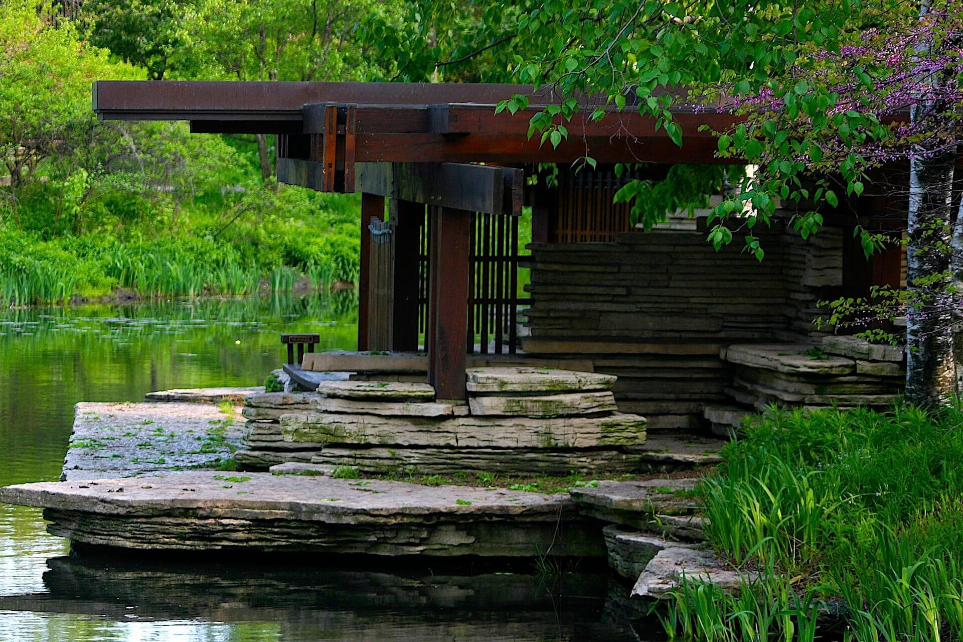 Prairie-style stone pavilion alongside a tranquil pond, surrounded by lush greenery at Alfred Caldwell Lily Pool in Chicago’s Lincoln Park.