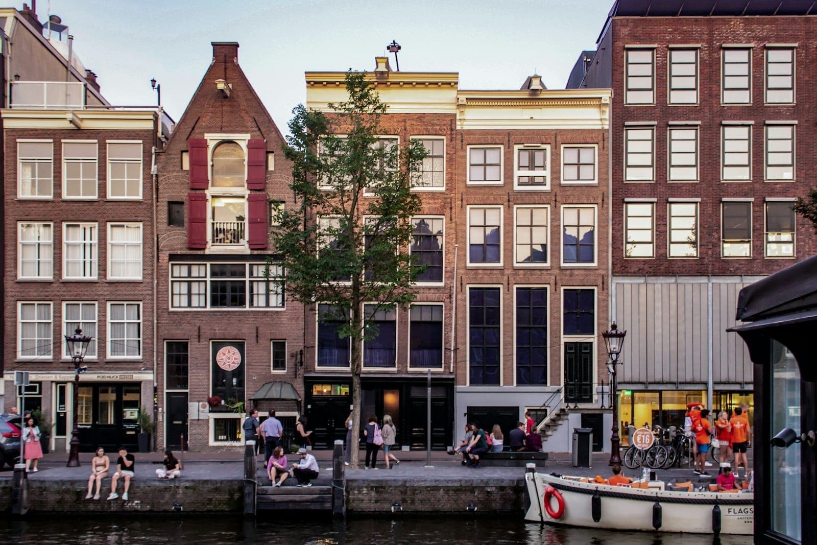 Frontansicht der Grachtenhäuser in Amsterdam mit Menschen, die sich neben dem Anne Frank Haus versammeln, und zeigt einen wichtigen Ausschluss für Besucher.