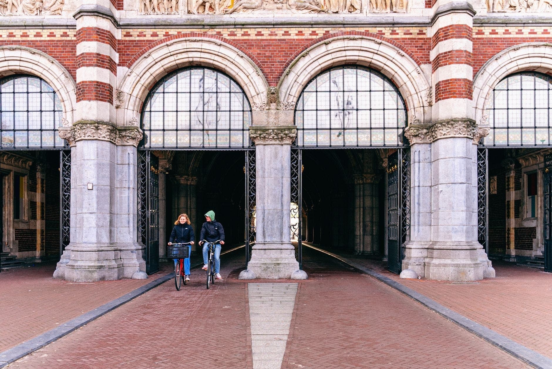 Zwei Radfahrer fahren unter dem Bogengang des Rijksmuseums in Amsterdam hindurch, einem ikonischen Wahrzeichen am Museumplein.