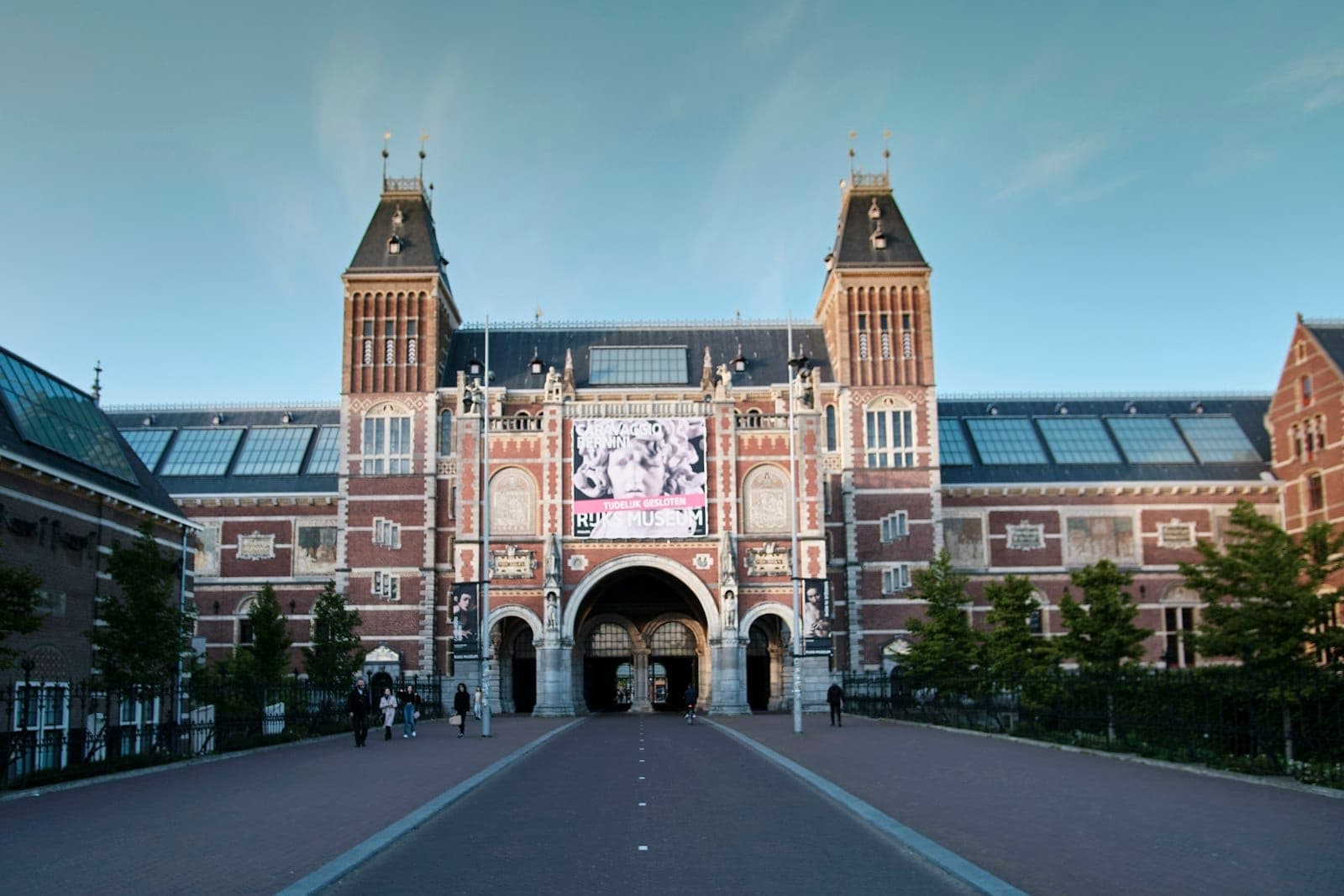 Weitwinkelansicht des Eingangs des Rijksmuseums in Amsterdam, mit Menschen, die an einem klaren Tag davor spazieren.