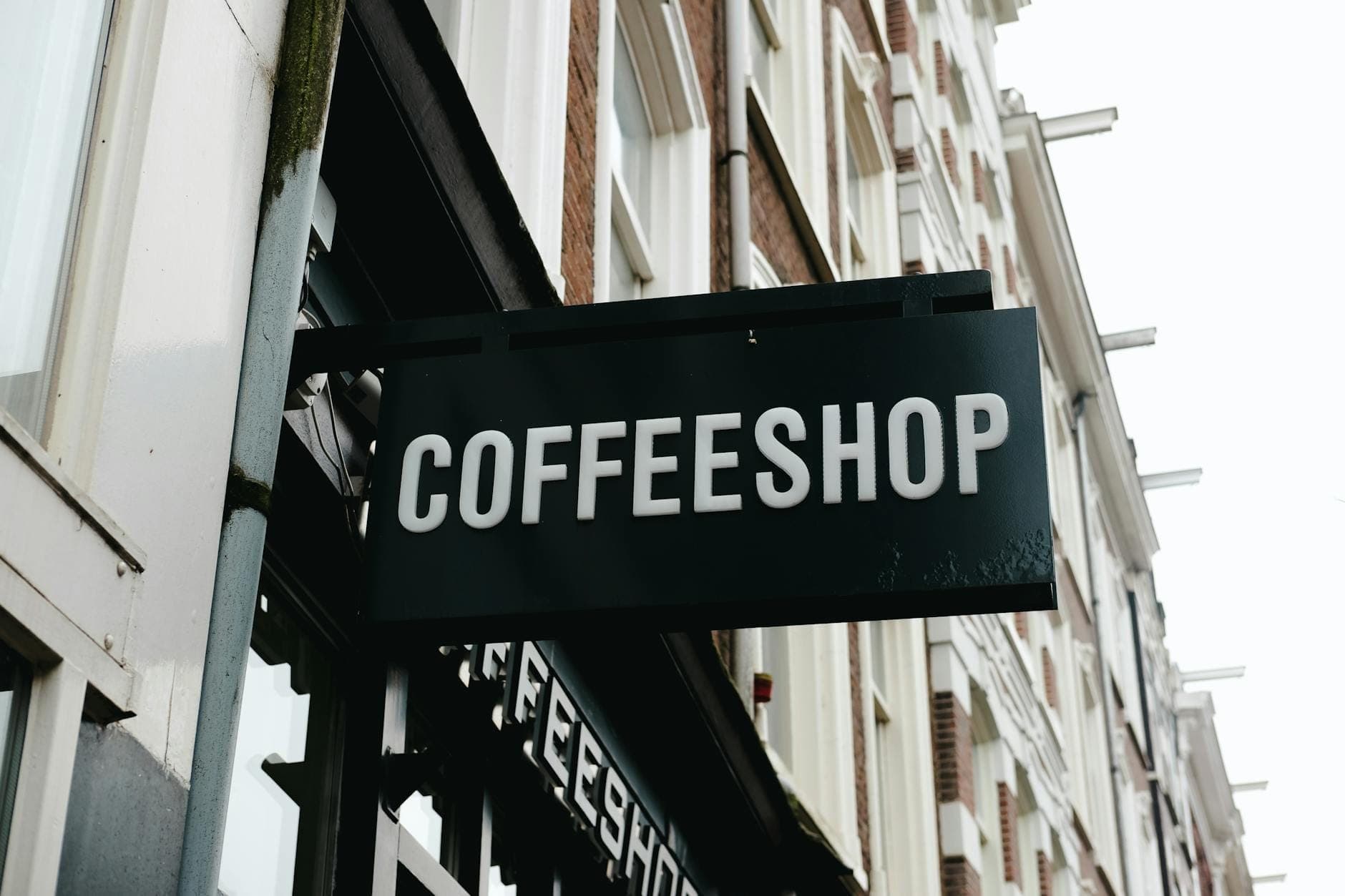 Straßenansicht eines Gebäudes in Amsterdam mit einem schwarzen Schild mit der Aufschrift 'COFFEESHOP' in großen weißen Buchstaben.