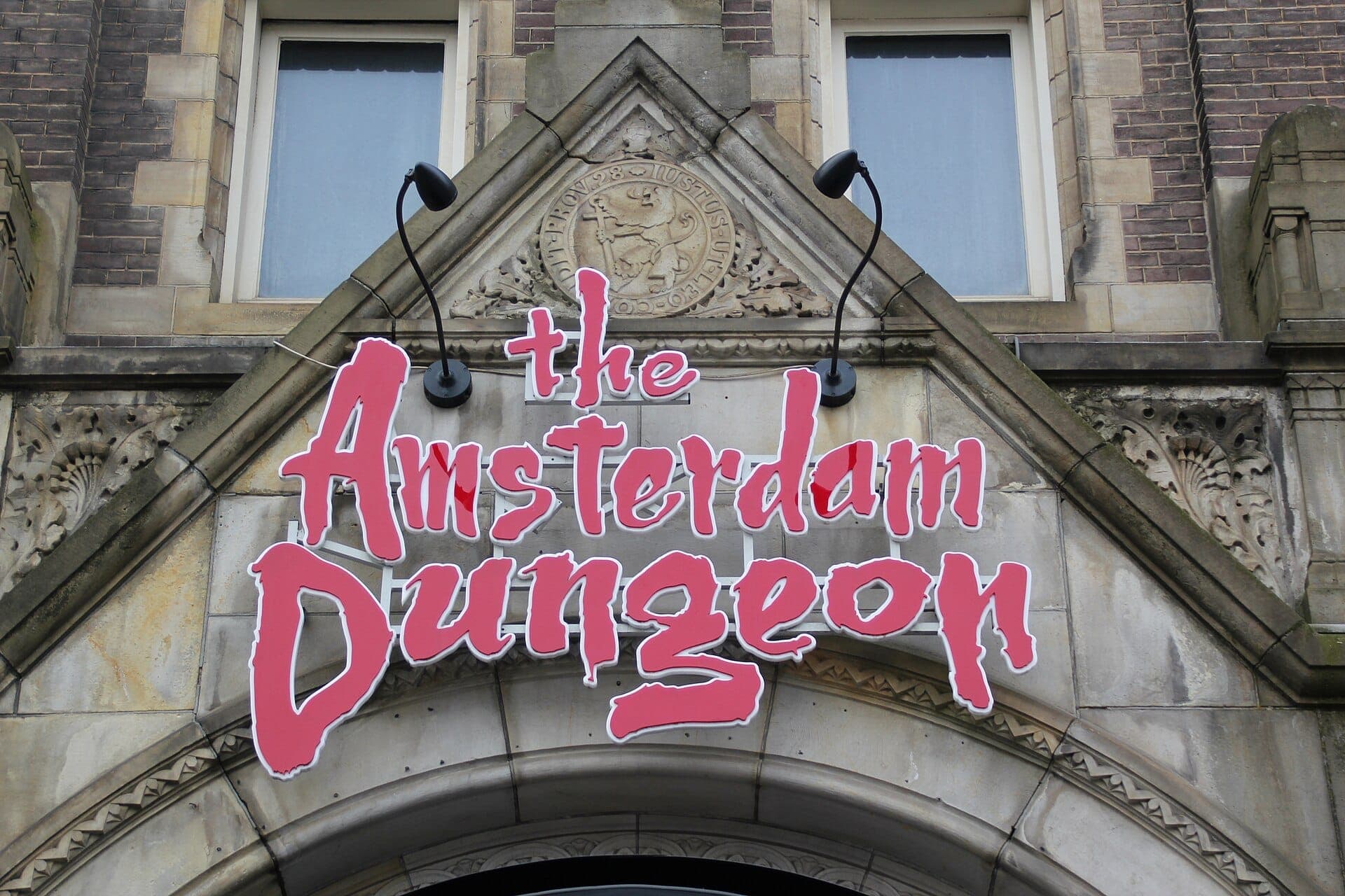 El cartel del Amsterdam Dungeon con letras rojas en negrita sobre la entrada arqueada de piedra de un edificio histórico en Rokin.
