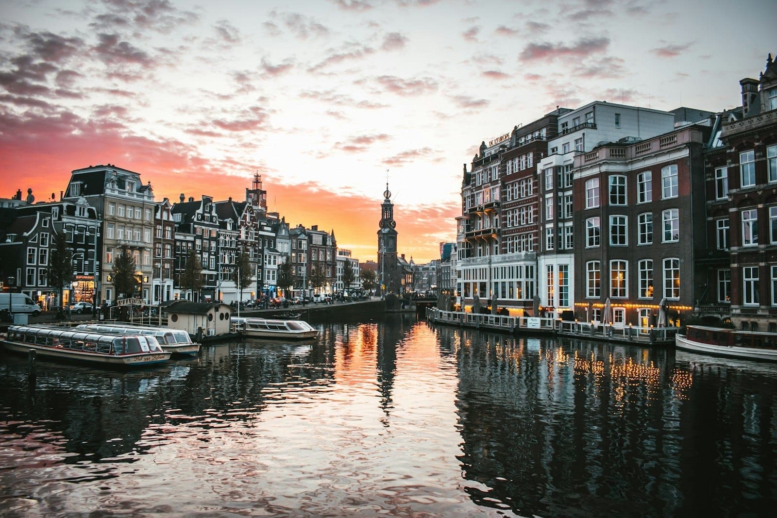 Romantischer Sonnenuntergang über einem Amsterdamer Grachtenkanal mit historischen Giebelhäusern, Booten und goldenen Spiegelungen im Wasser – eine einladende Kulisse für Paare.
