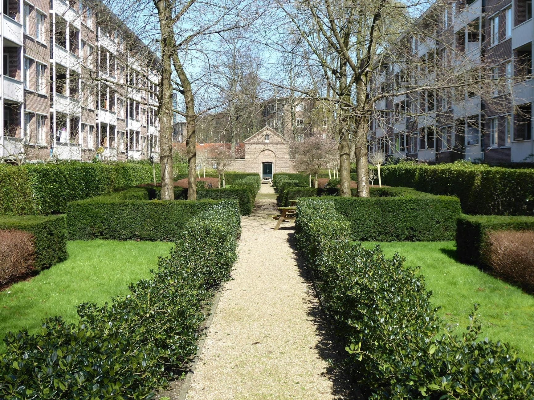 Grüner Hofgarten, flankiert von kanalartigen Apartmentgebäuden in Amsterdam, der zu einem kleinen Backsteinkapelleneingang führt.