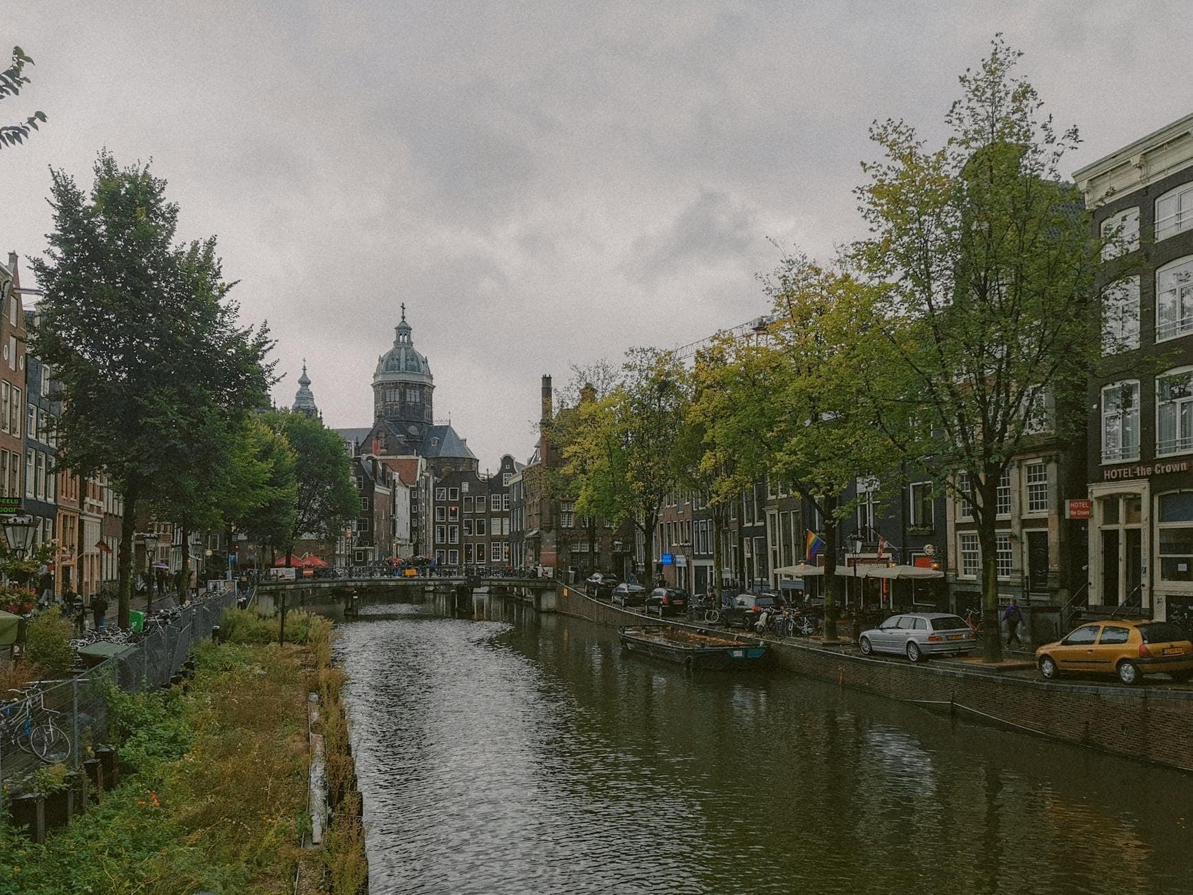 Bewölkter Herbsttag in Amsterdam mit bedecktem Himmel, Kanalblick, historischen Gebäuden und Bäumen mit frühem Herbstlaub.