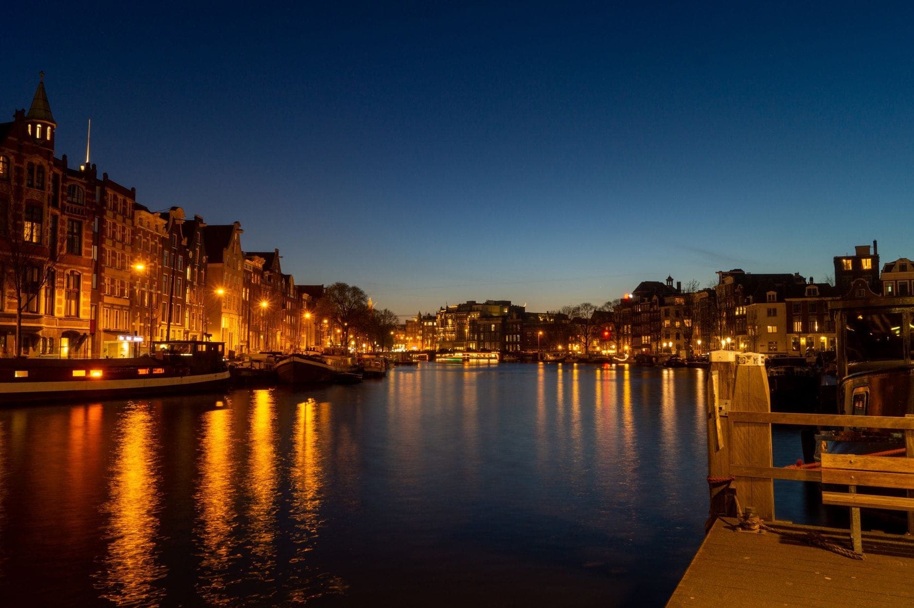 Amsterdamer Gracht in der Abenddämmerung mit festlichen Winterlichtern, die sich im ruhigen Wasser spiegeln – eine magische Winteratmosphäre.