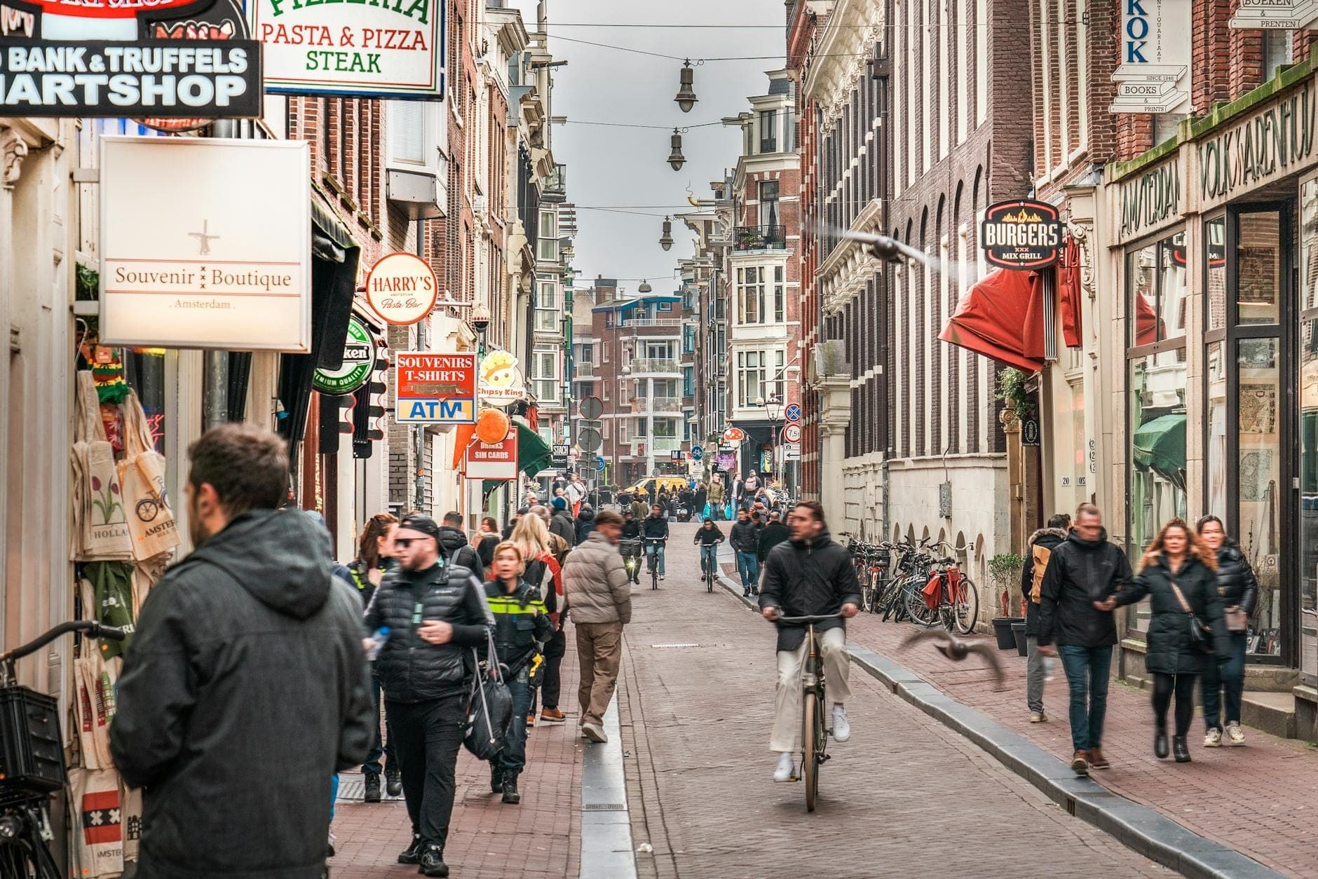 Belebte Straße in Amsterdam mit Geschäften, Radfahrern und Fußgängern an einem bewölkten Wintertag.