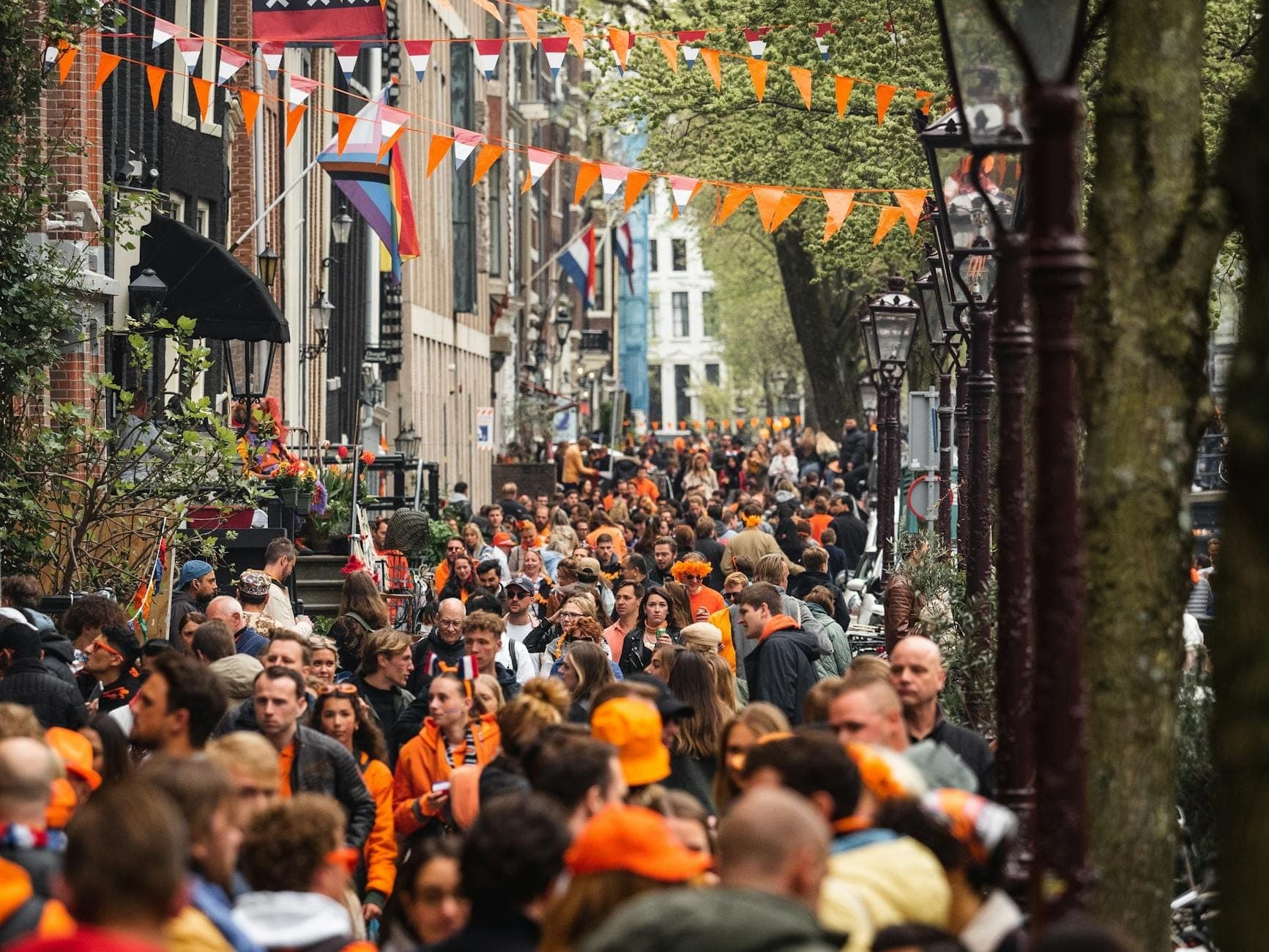 Eine überfüllte Amsterdamer Straße voller Menschen in Orange, festliche Banner hängen über den Köpfen – pure Königstag-Stimmung.