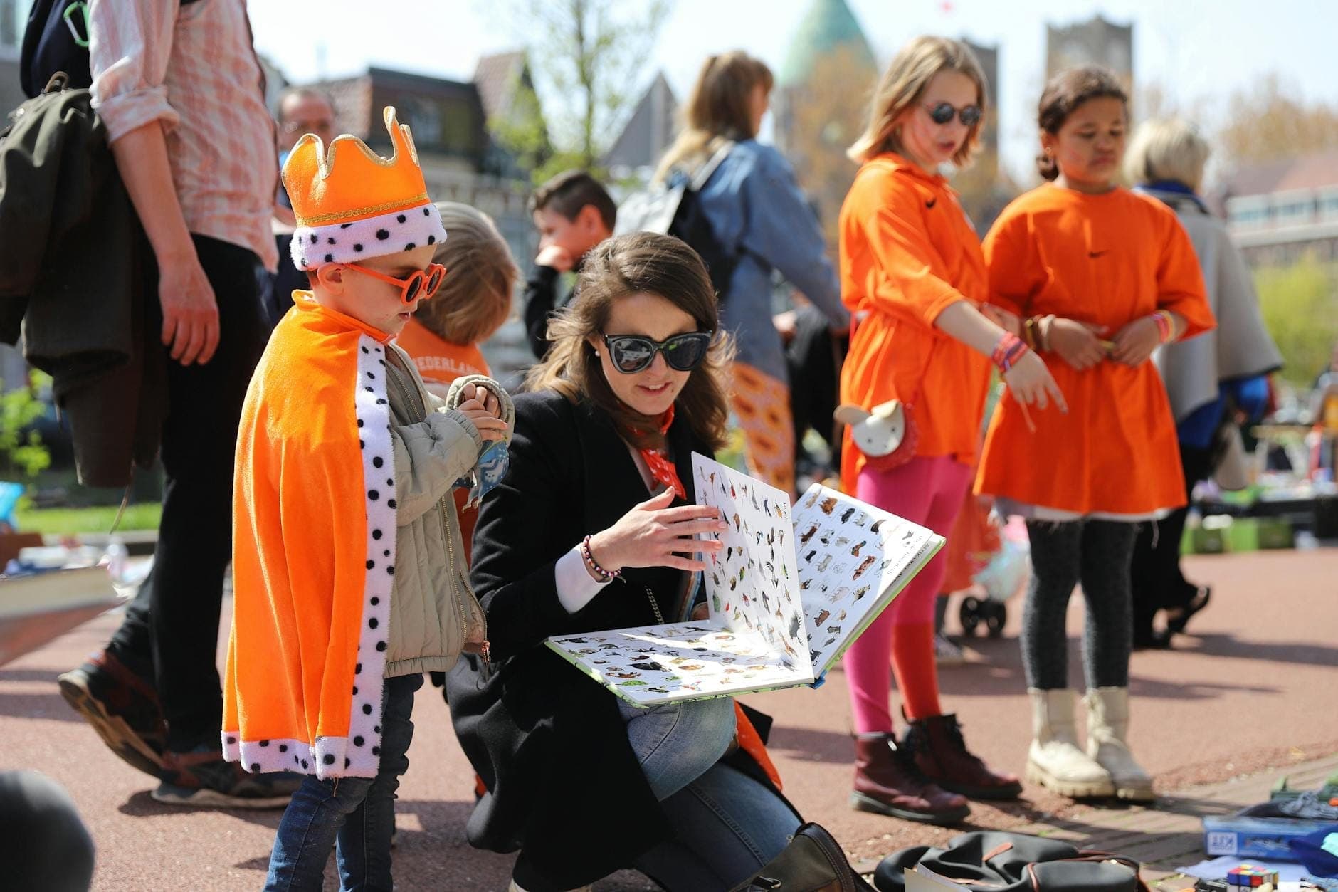 Menschen in orangefarbener Kleidung, die im Freien Artikel durchstöbern und verkaufen, wahrscheinlich während der Feierlichkeiten zum Koningsdag in Amsterdam.