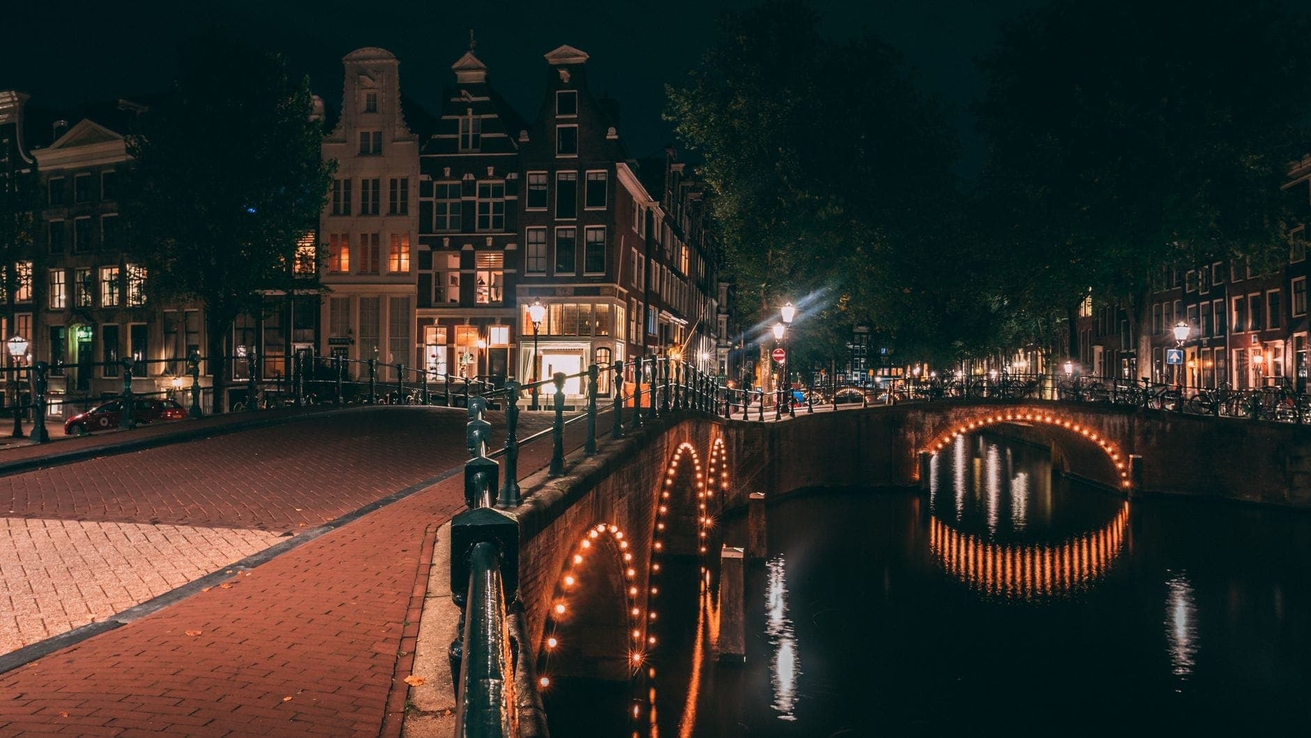 Nächtlicher Blick auf einen beleuchteten Amsterdamer Kanal mit ikonischen Brücken und historischen Gebäuden, die die lebhafte Nachtleben-Atmosphäre der Stadt widerspiegeln.