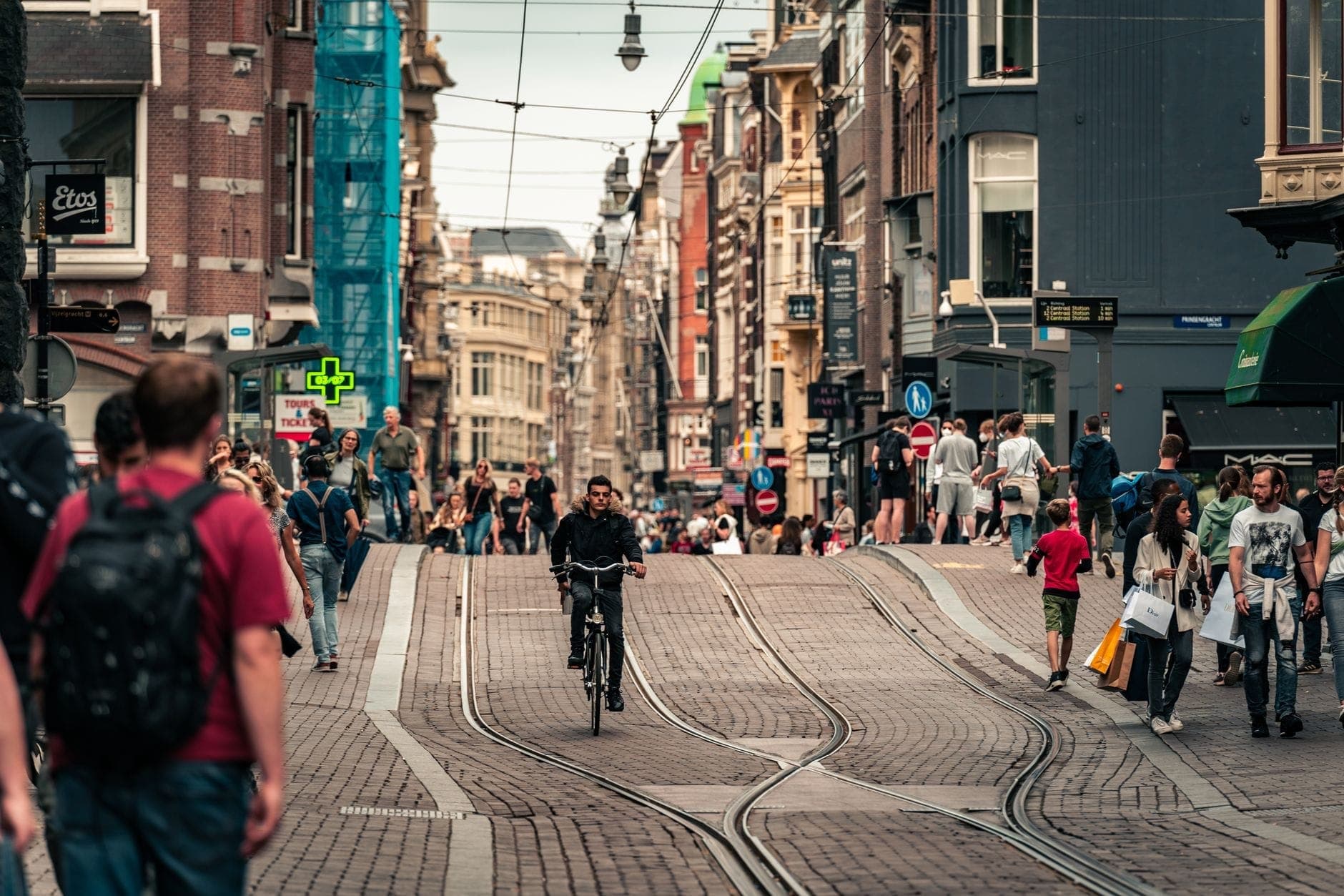 Belebte Amsterdamer Straßenszene mit Radfahrern zwischen Fußgängern, Straßenbahnschienen und historischen Gebäuden – typisch für die lebhafte Fahrradkultur der Stadt.
