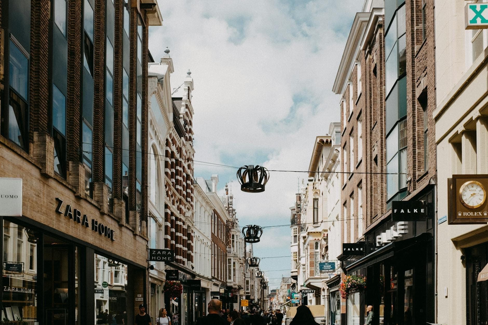 Belebte Amsterdamer Einkaufsstraße gesäumt von Boutiquen, mit flanierenden Menschen unter einem strahlend blauen Himmel mit vereinzelten Wolken.