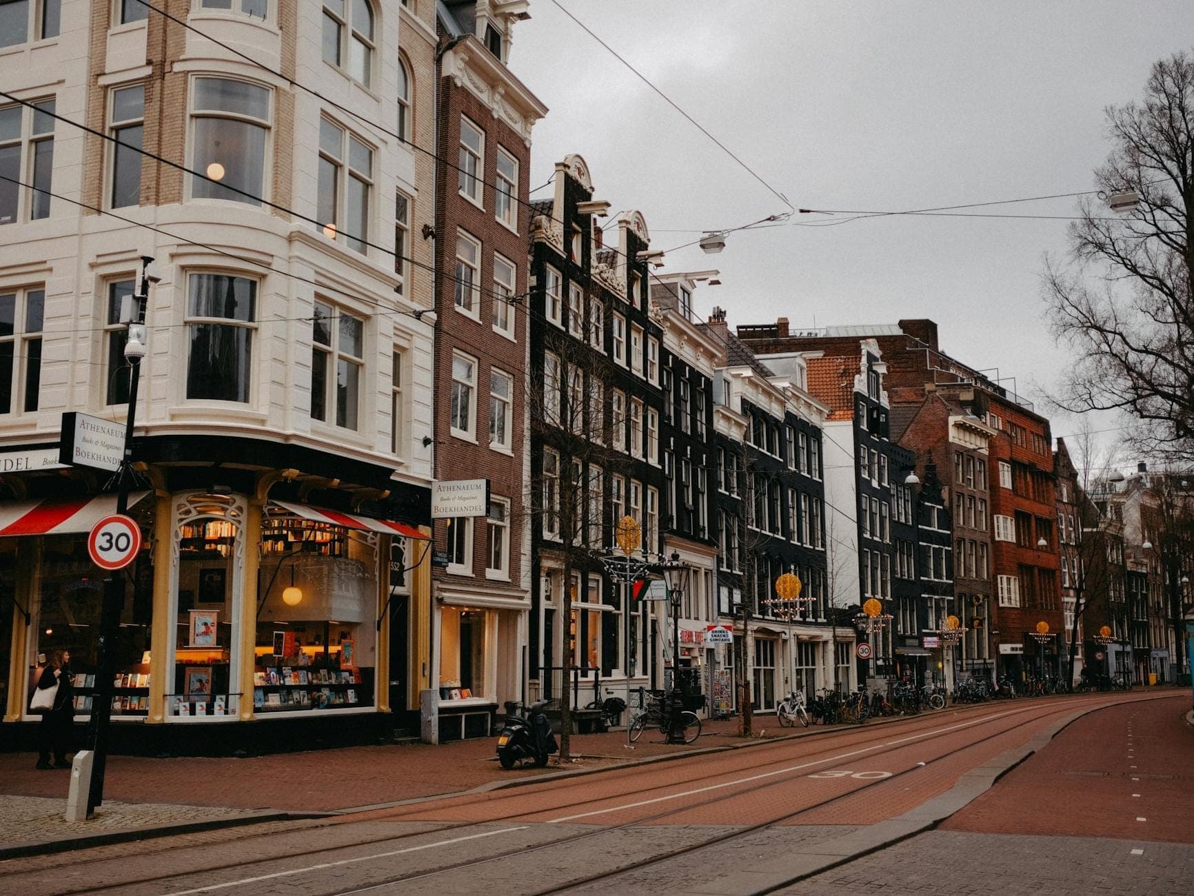 Straßenansicht von Amsterdam mit klassischen niederländischen Gebäuden, Straßenbahnlinien und einem Eckladen, der die lebhafte Atmosphäre eines Einkaufsviertels vermittelt.