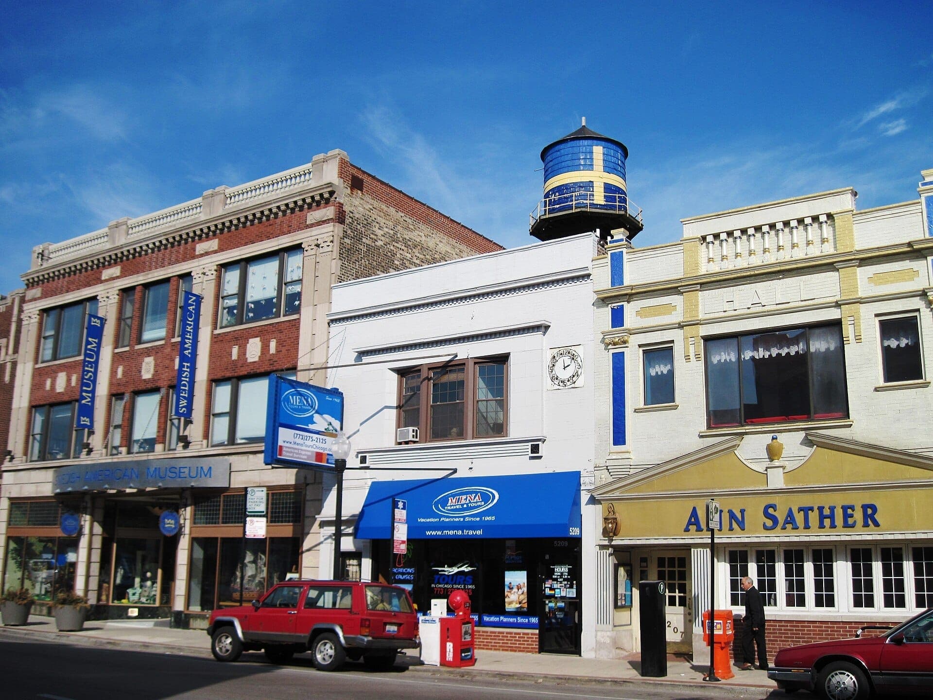 Historic storefronts and colorful water tower in Chicago's Andersonville Shopping District, featuring Swedish American Museum and local businesses under a clear sky.