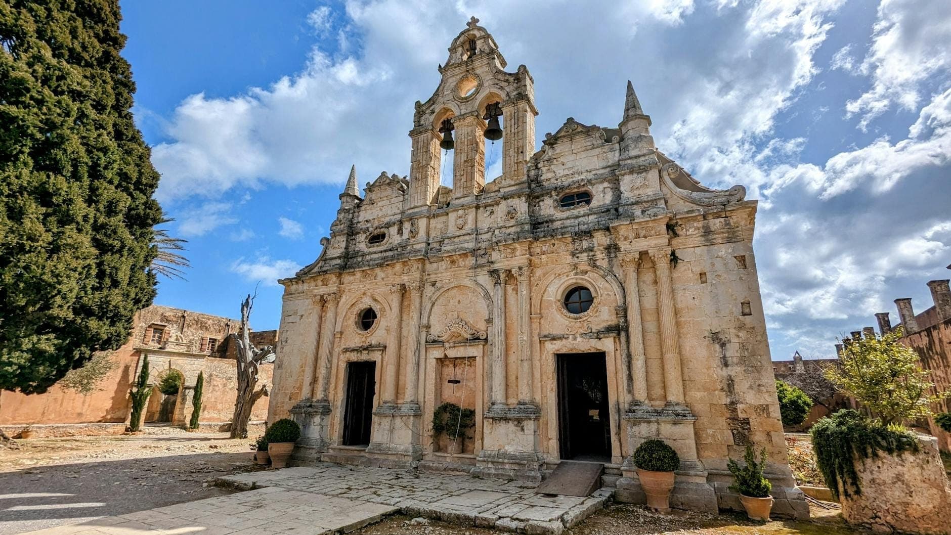 Die reich verzierte Steinfassade des Klosters Arkadi auf Kreta, eingerahmt von Zypressen und dramatischem Himmel, mit detailreicher Architektur und historischem Charakter.