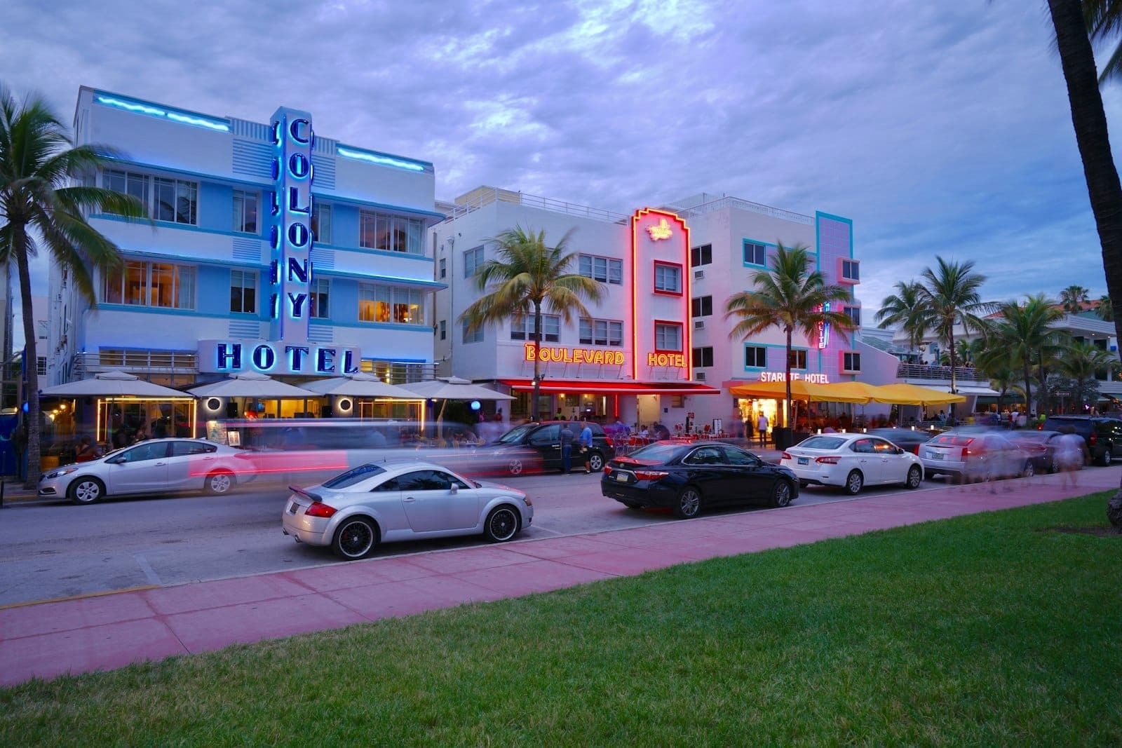 Hôtels Art Déco le long d'Ocean Drive à Miami Beach au crépuscule avec des néons, des palmiers et des voitures garées le long de la rue.