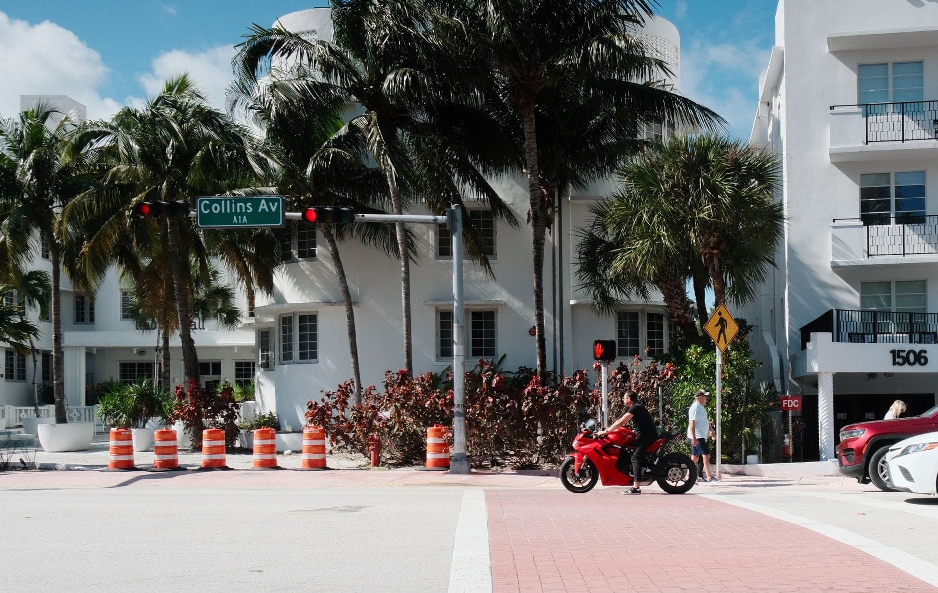 Scène de rue à Miami Beach avec le panneau Collins Ave, des palmiers, des personnes traversant et des bâtiments Art Déco en arrière-plan.
