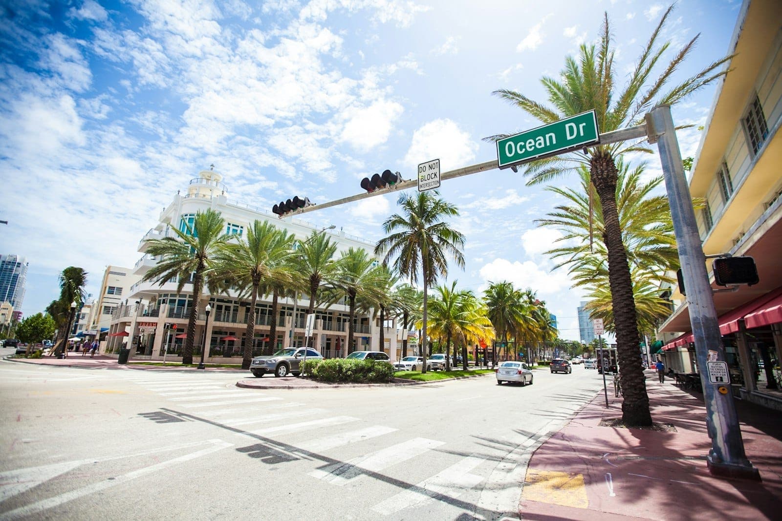 Vue large d'Ocean Drive à Miami Beach avec des palmiers, des bâtiments Art Déco classiques et un panneau de rue bien visible par une journée ensoleillée.