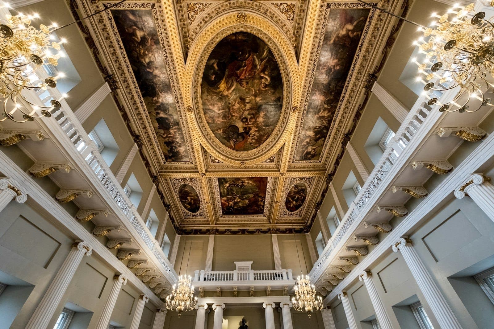 Wnętrze Banqueting House z imponującym malowanym sufitem autorstwa Rubensa, białymi kolumnami, złotymi akcentami i ozdobnymi żyrandolami.