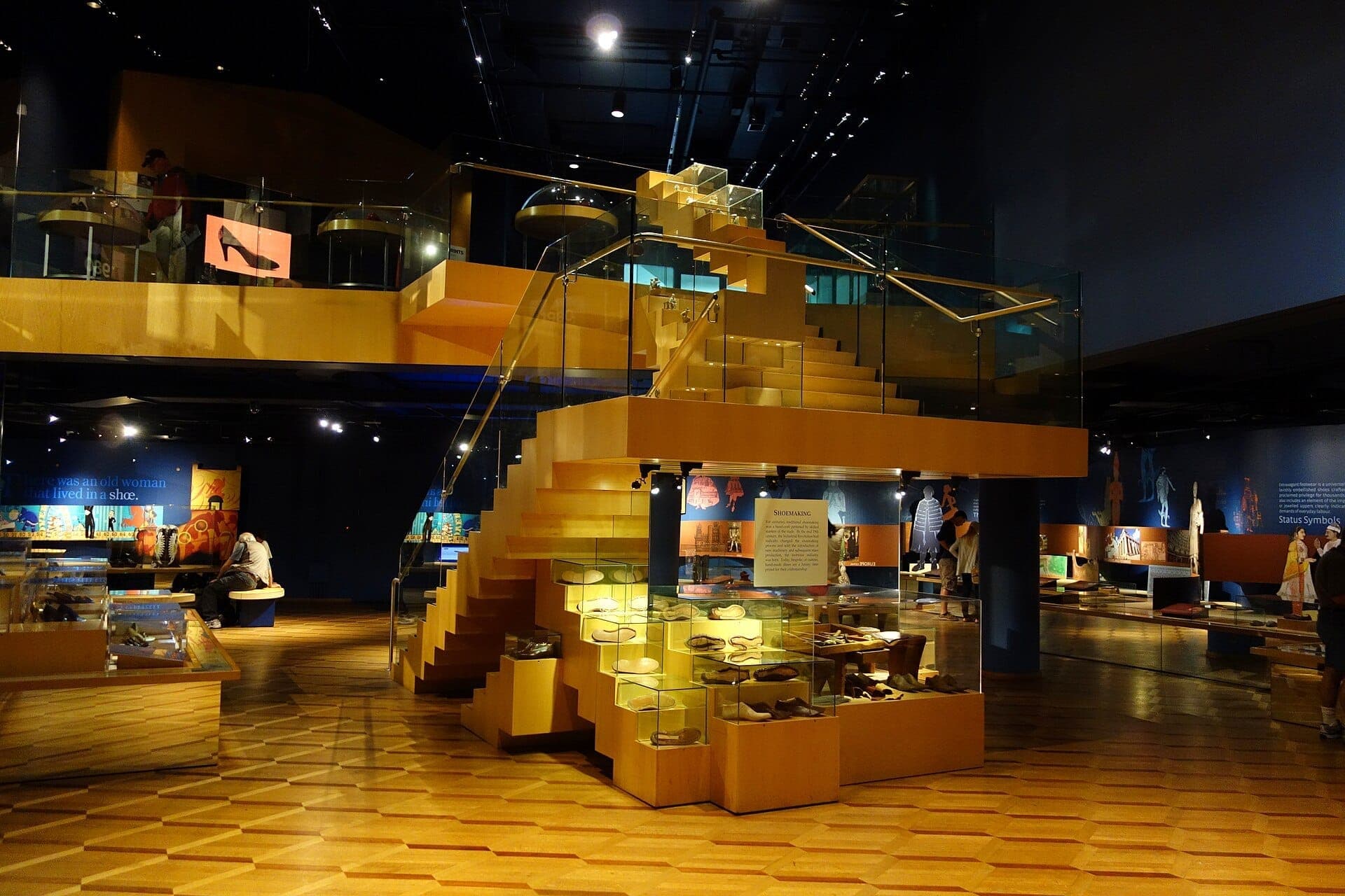 Vista interna del Bata Shoe Museum con scale in legno, vetrine per scarpe in vetro e visitatori che esplorano lo spazio espositivo ben illuminato.