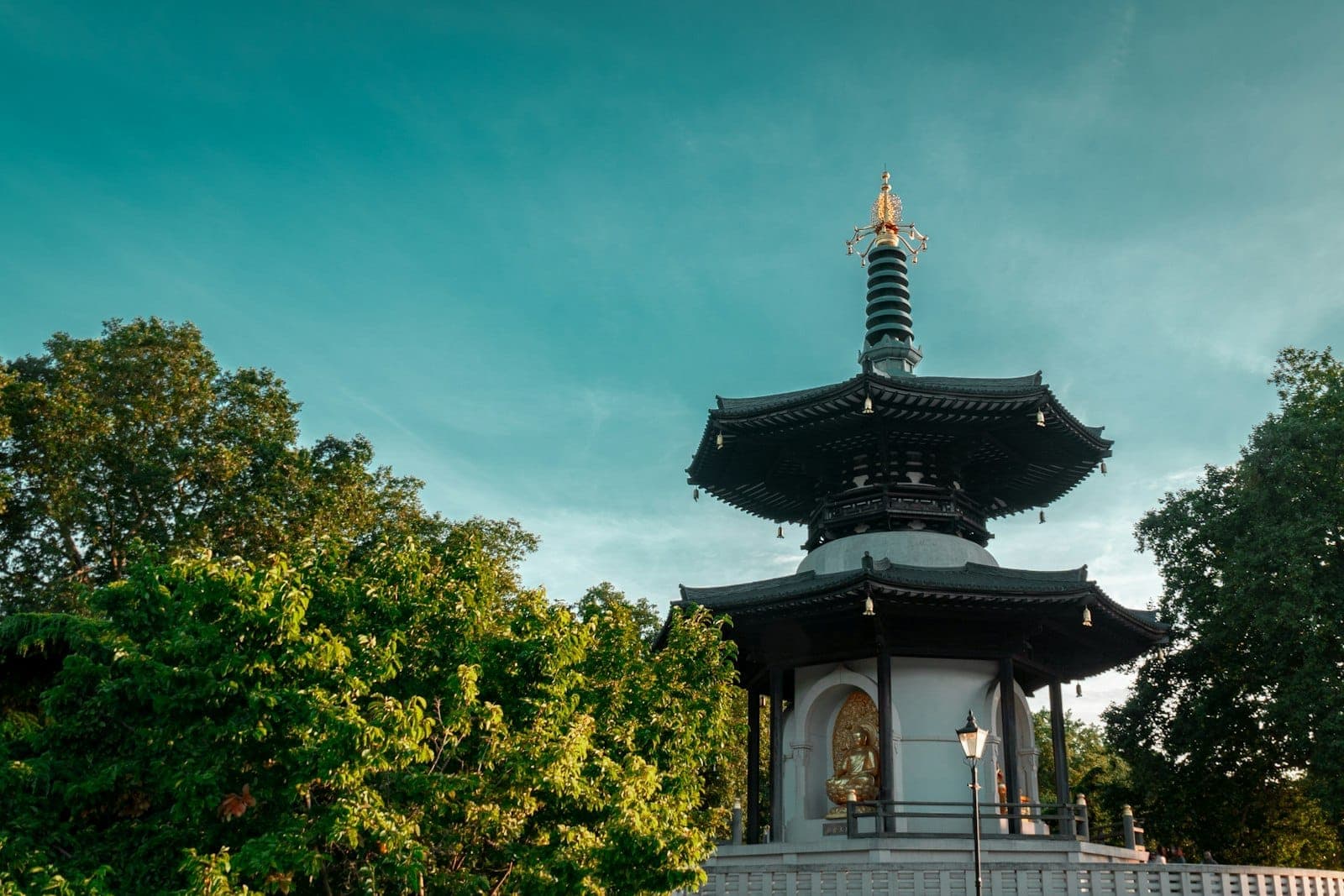 Buddhist Peace Pagoda im Battersea Park, London, umgeben von grünen Bäumen unter einem klaren blauen Himmel mit goldenem Sonnenlicht.