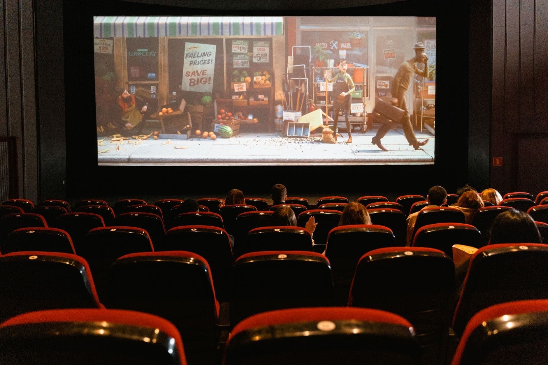 Rows of red velvet cinema seats with people watching a film on a large screen in a classic movie theater setting.